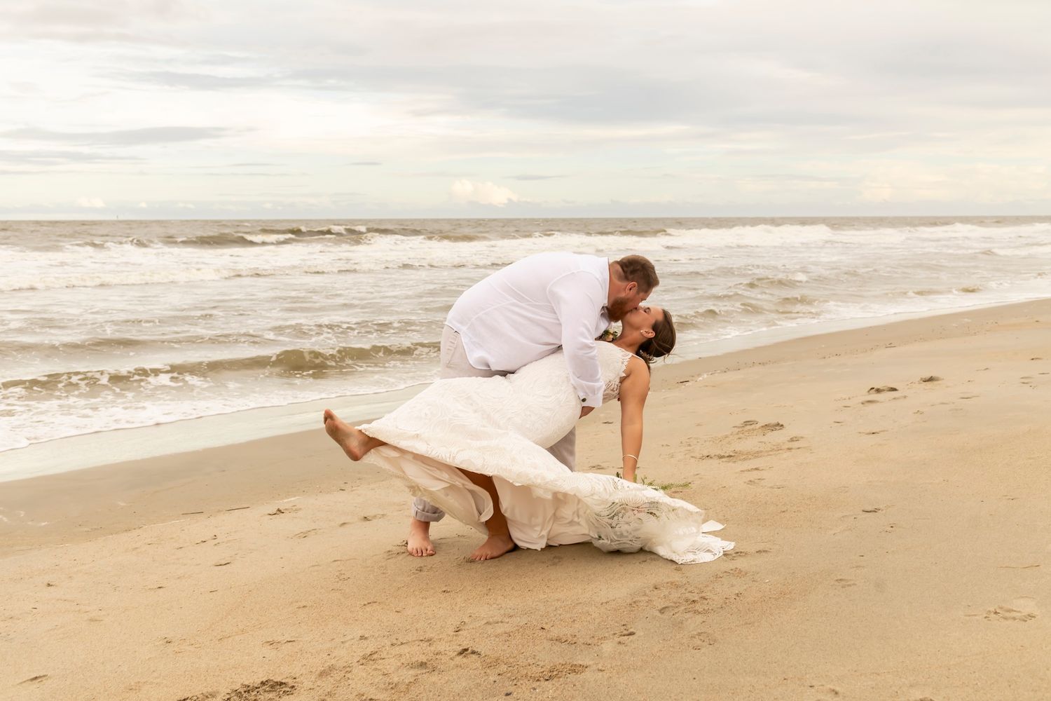 A couple shares a romantic moment on a cloudy beach as waves roll in along the shoreline.