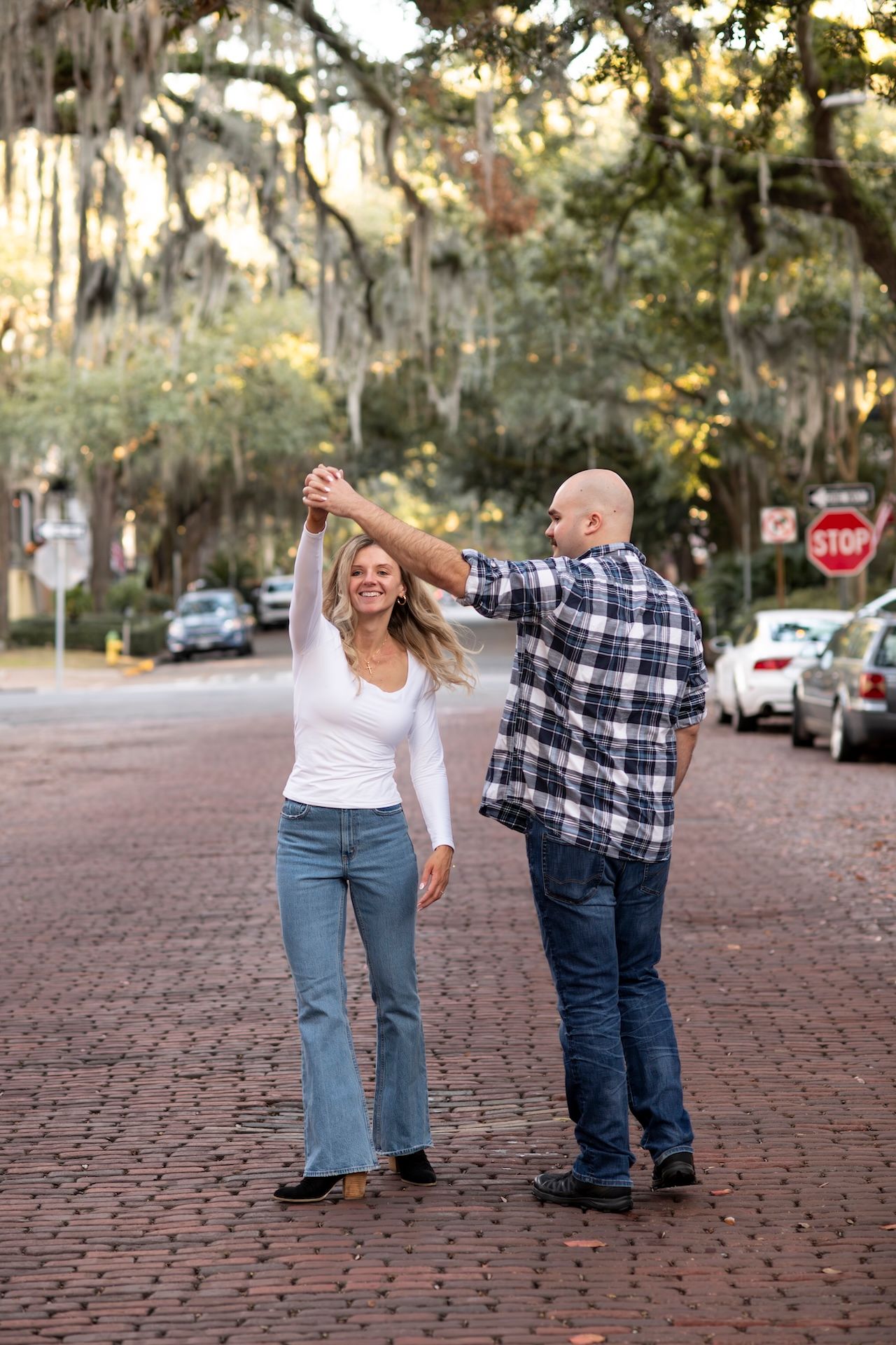 A couple dances together on a brick-paved street lined with Spanish moss-draped trees in a romantic Southern setting.