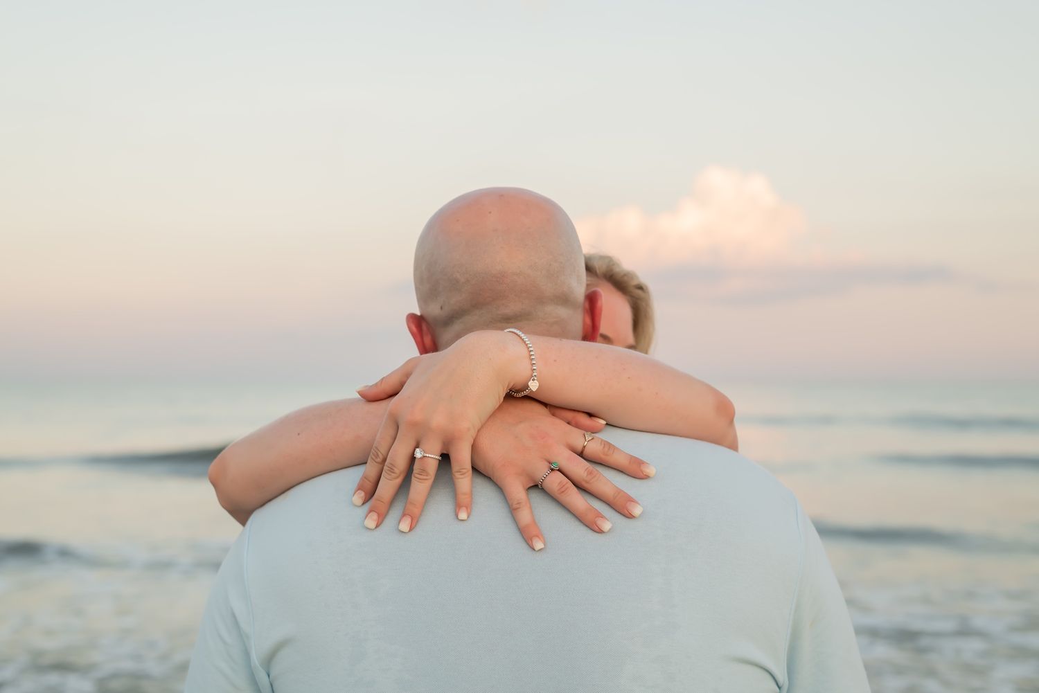 Close-up view of entwined hands against blurred beach sunset background showing intimacy and romance.