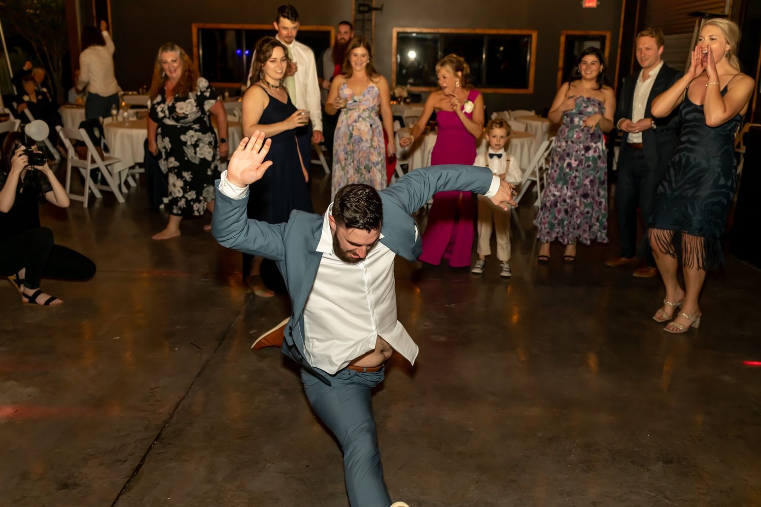 A group of party guests dancing energetically at a reception venue with low lighting.