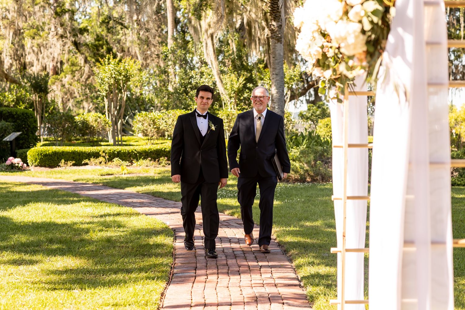 An outdoor wedding venue with white columns and Spanish moss draped trees creates a romantic scene.