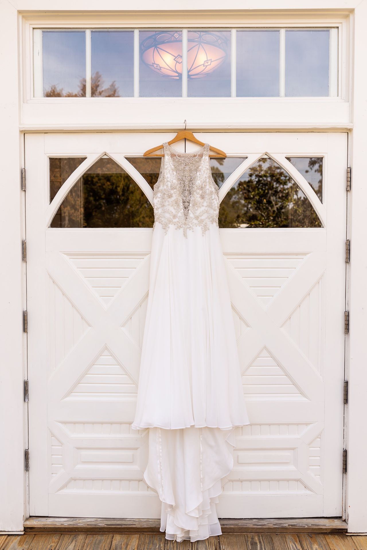 White wedding dress hanging on a hanger against white panel doors in natural light.