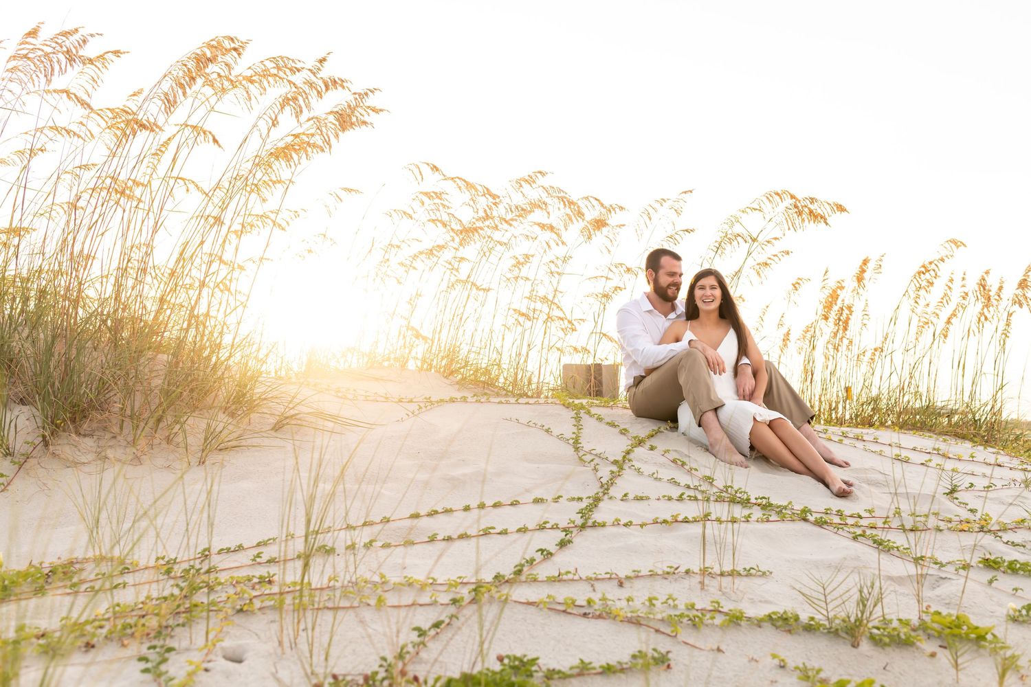 Wedding couple embraces on a sandy beach at sunset with golden sea oats swaying in the breeze.