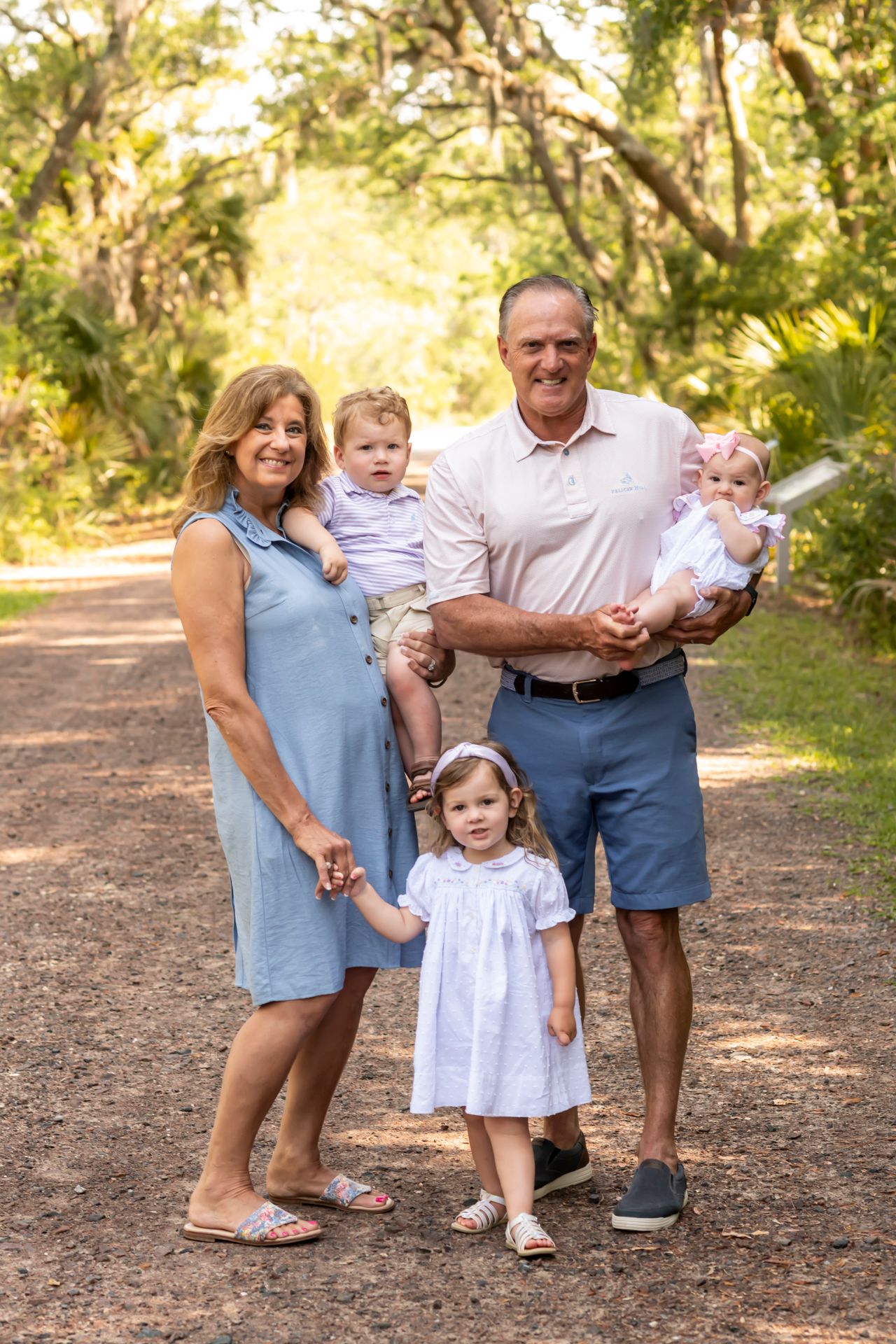 Family portrait session on a sunlit wooded path showing warm interactions between three generations on a summer day.