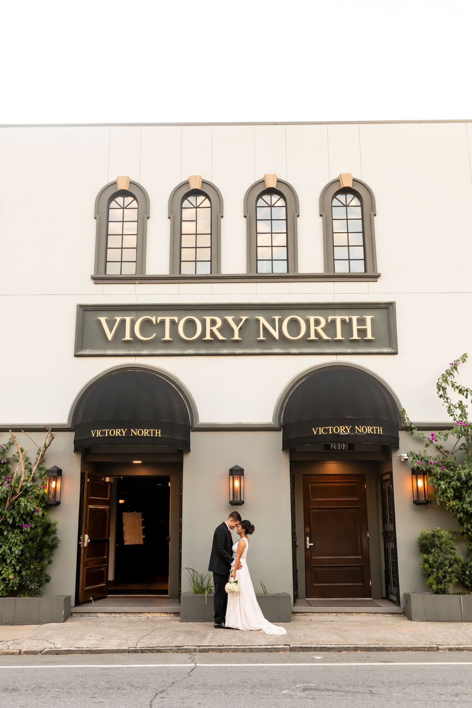 A couple stands at the entrance of Victory North, an elegant white building with arched windows.