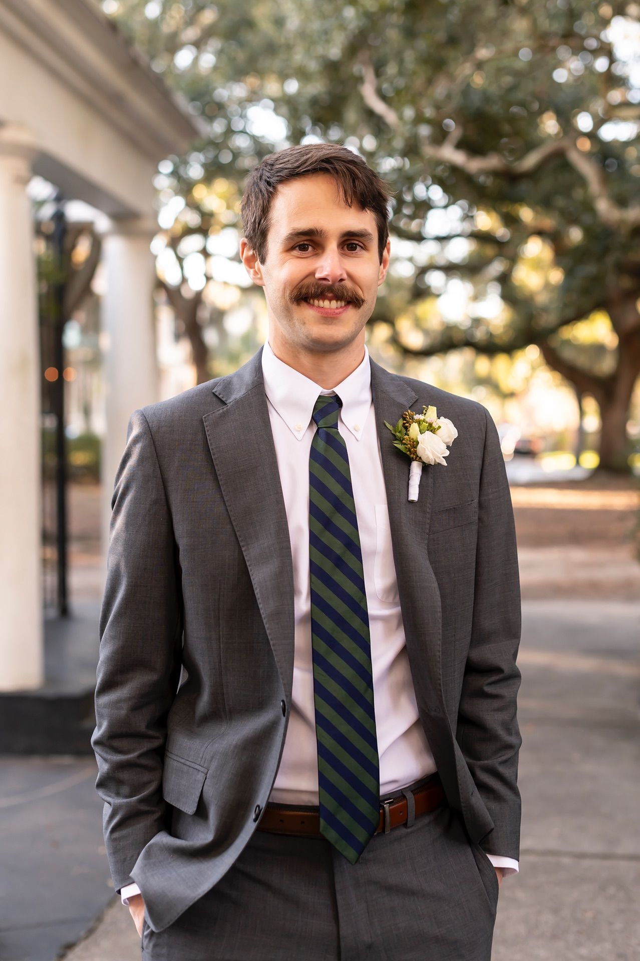 Dapper person in dark suit and striped tie poses casually in a series of outdoor portraits with columns visible.