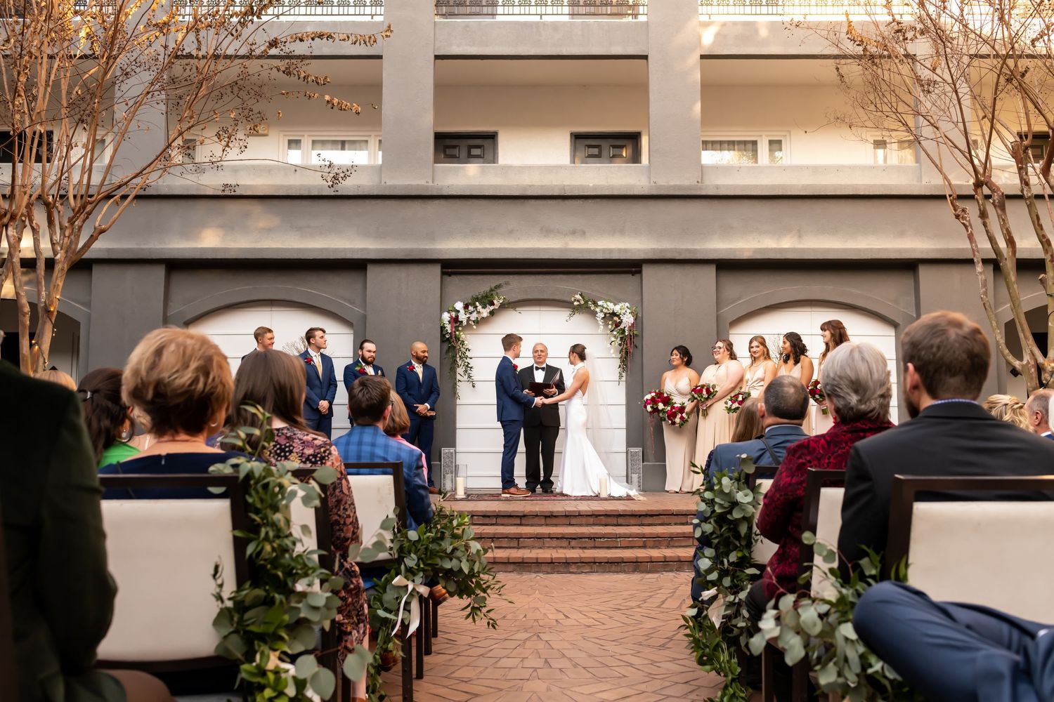 People gather in an elegant courtyard surrounded by white archways, columns and decorative greenery during an outdoor event.
