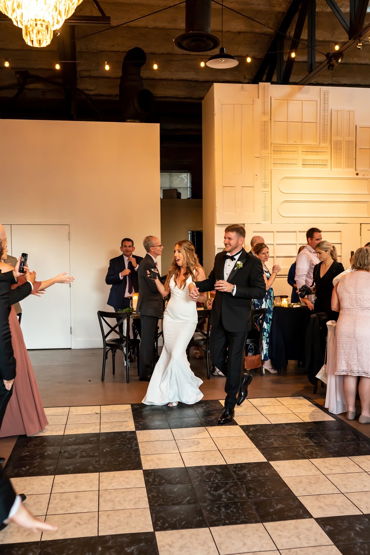 Wedding guests enjoying a fun line dance routine on a black and white checkered dance floor at an indoor reception.