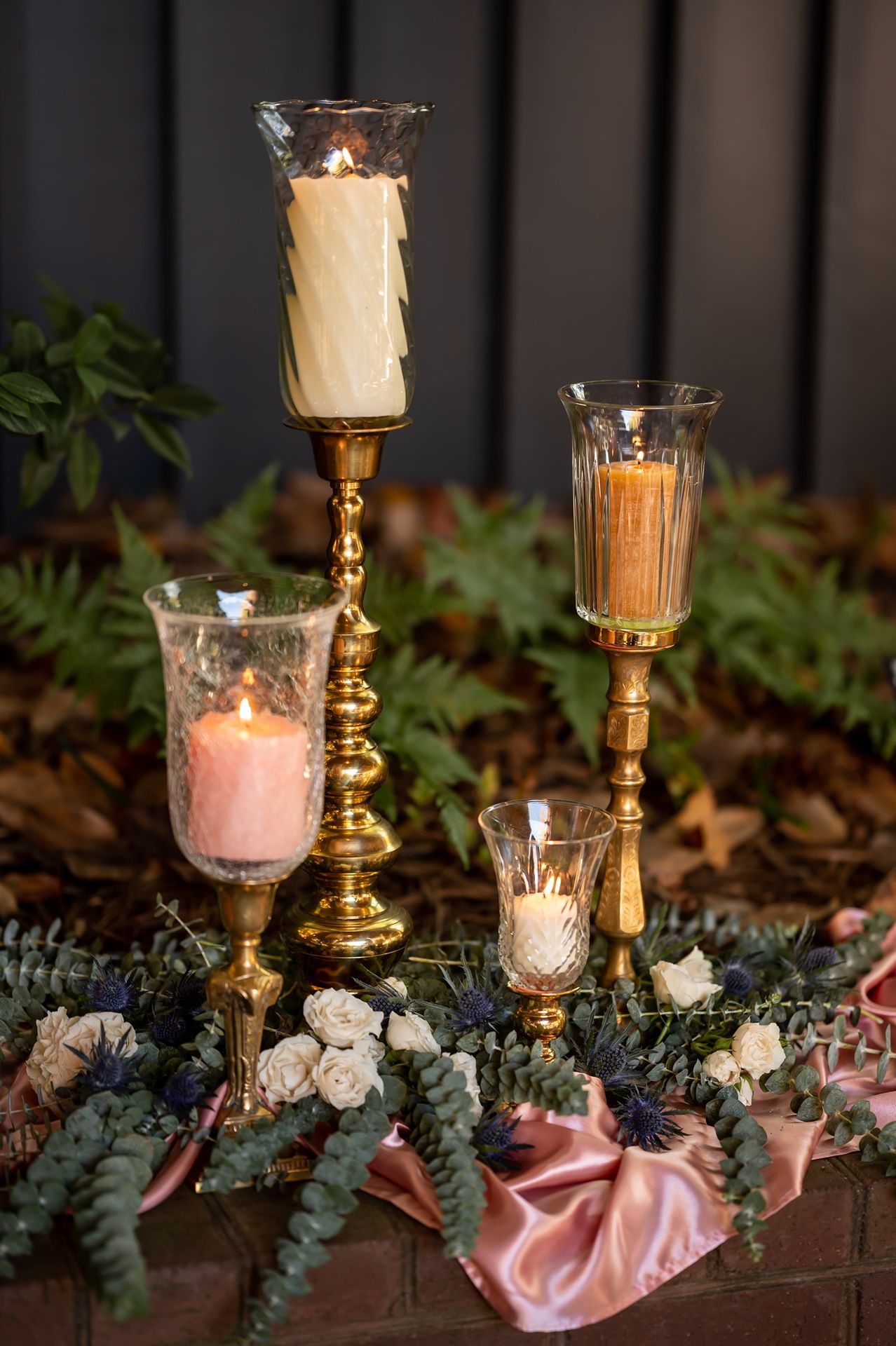 Elegant wedding decor featuring gold candlesticks with pink and cream candles surrounded by eucalyptus and white roses.