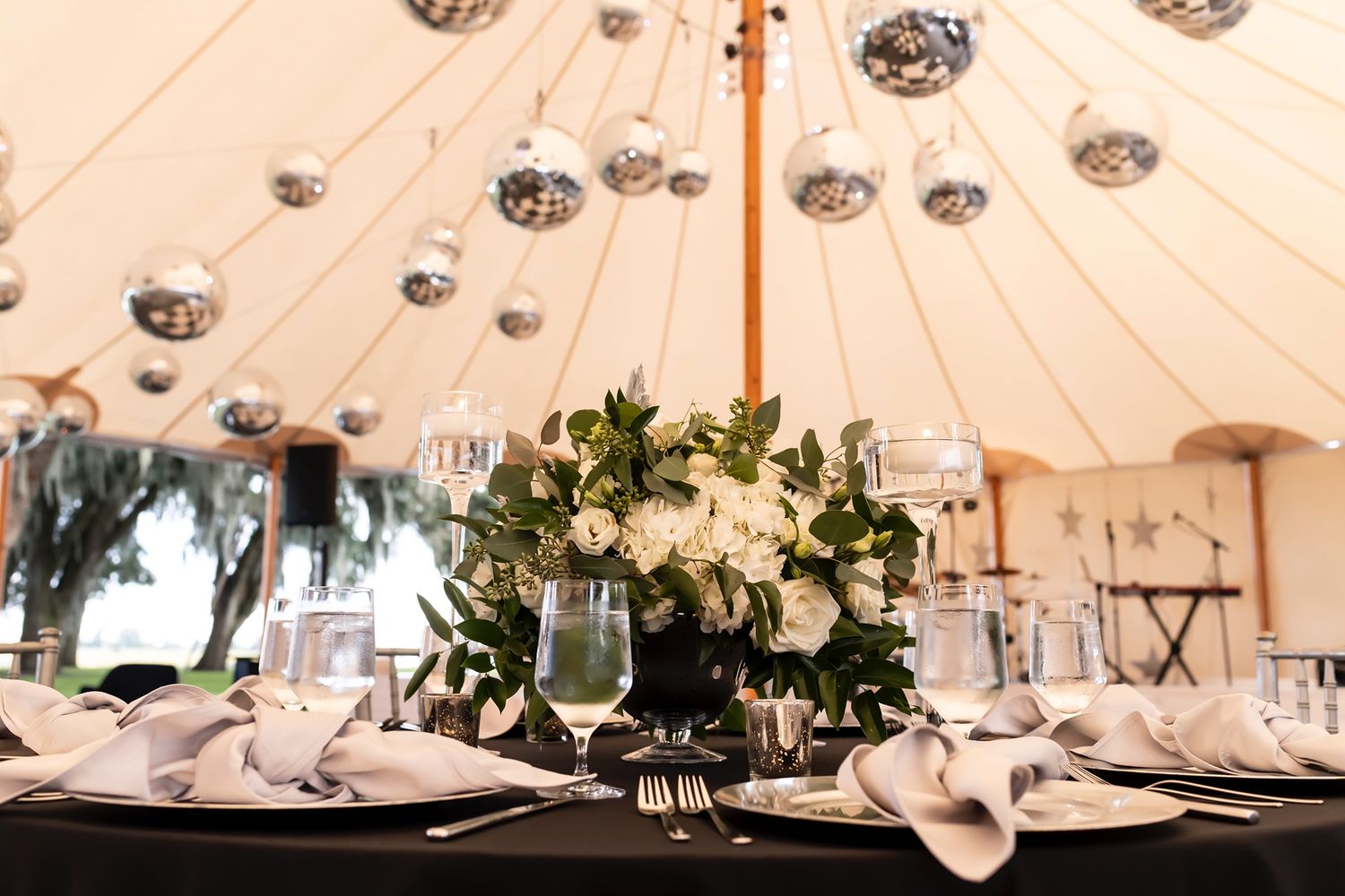 Elegant white wedding reception tent with round dining tables and hanging paper lanterns creating a romantic ambiance.
