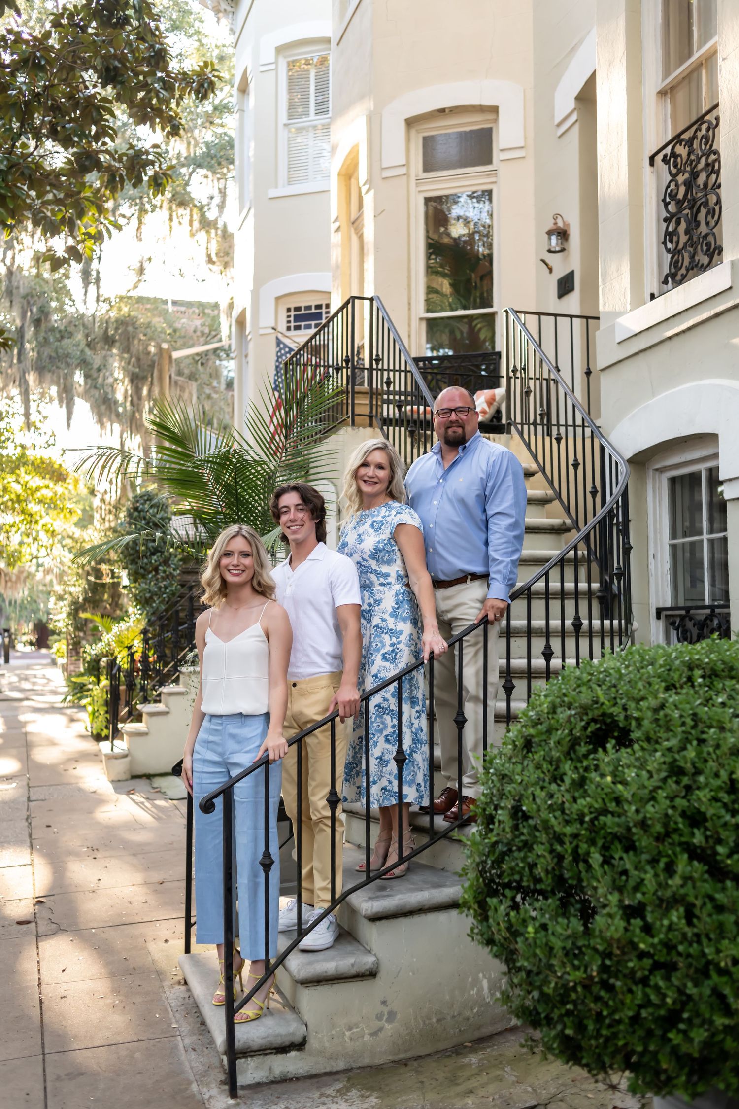 Group of people smiling and posing casually on the front steps of an elegant townhouse building.