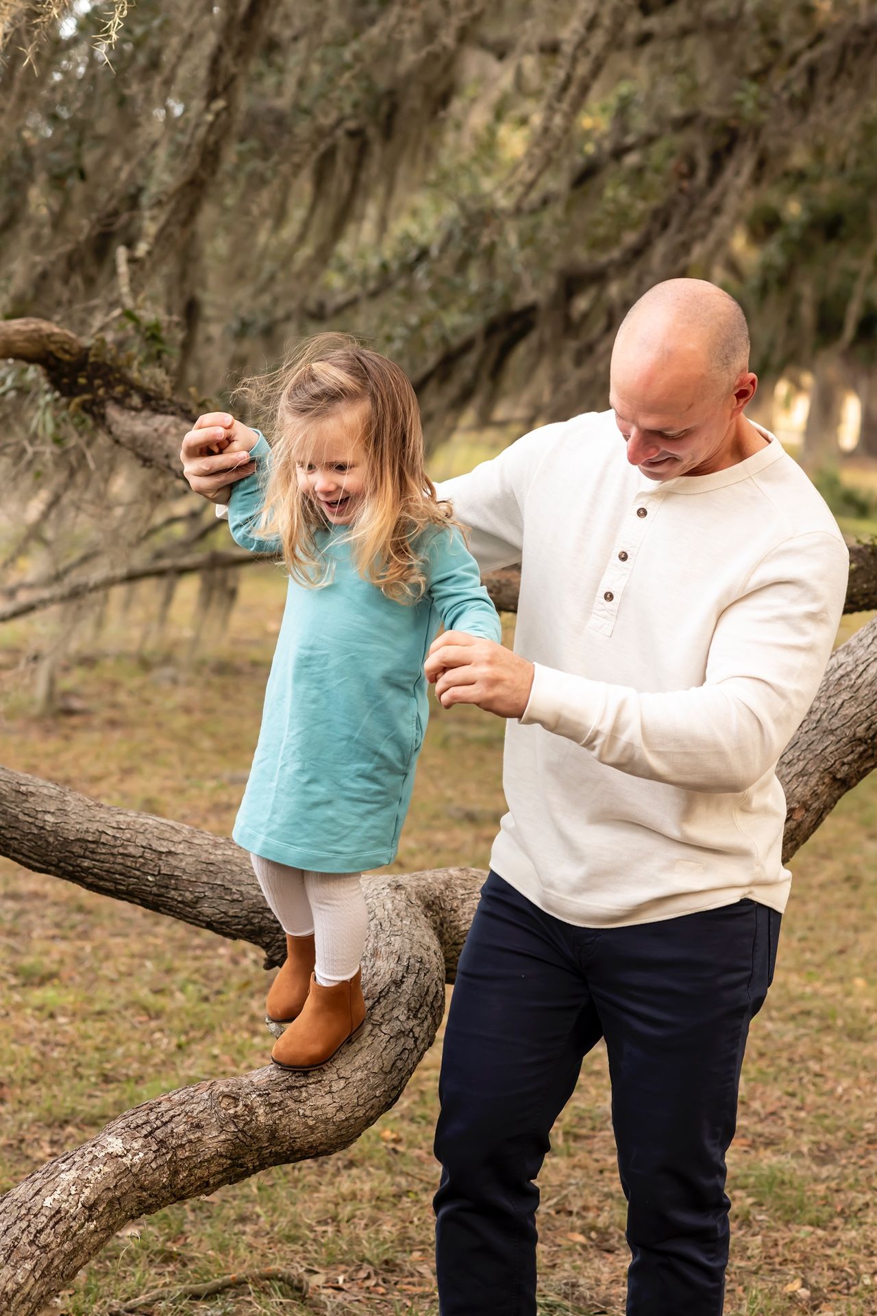 Two people enjoying a playful moment together on a fallen tree branch in a mossy forest setting.