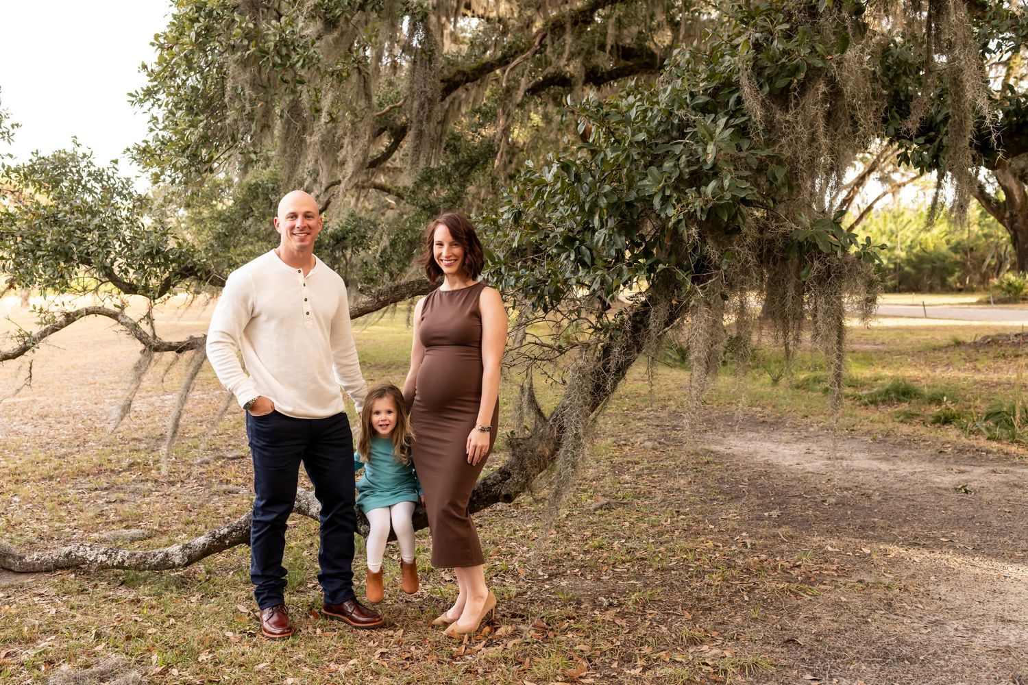 Family poses outdoors under Spanish moss draped trees at golden hour in a natural park setting.
