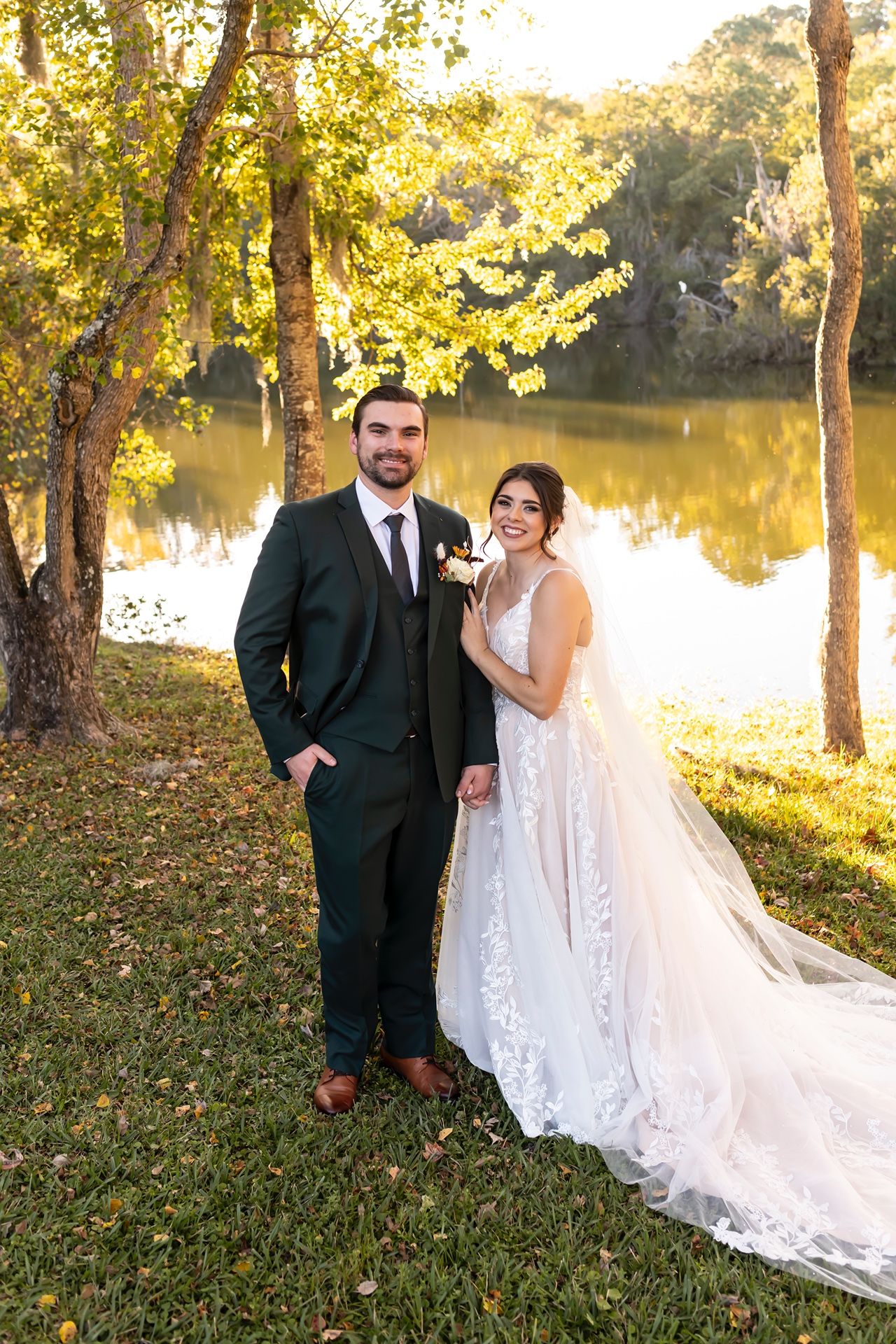 Wedding couple shares joyful moment near a scenic lake surrounded by autumn trees with golden sunlight.