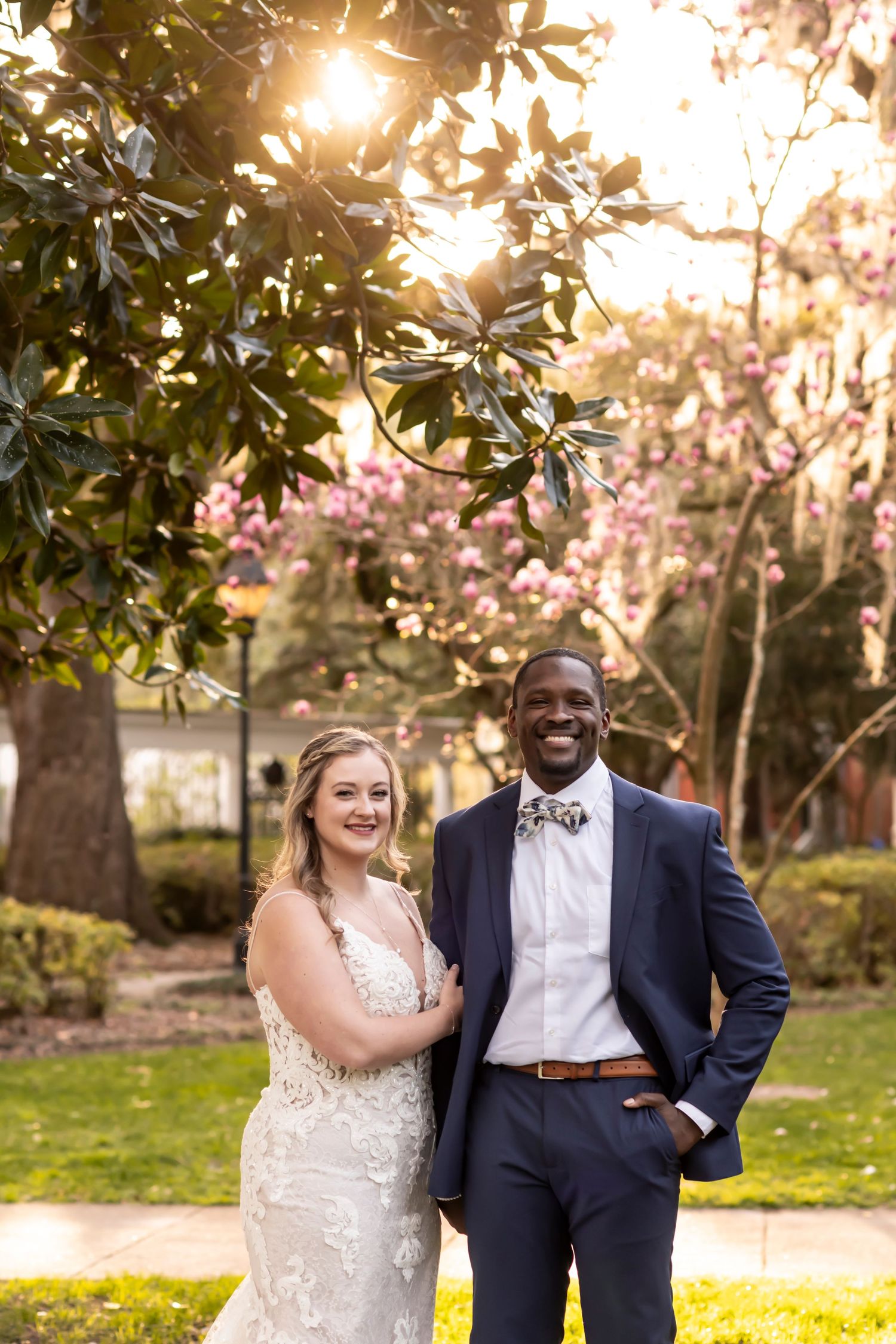 Happy couple shares joyful laughter under blooming spring trees during sunset wedding photoshoot.