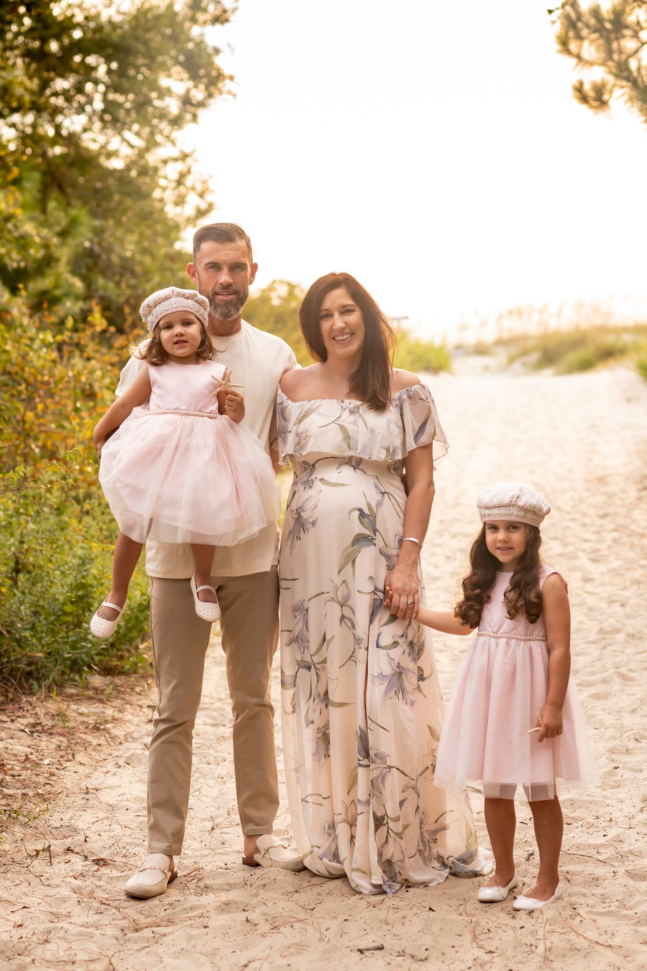 Family dressed in coordinating pink and beige outfits poses together on a nature path during golden hour sunset.