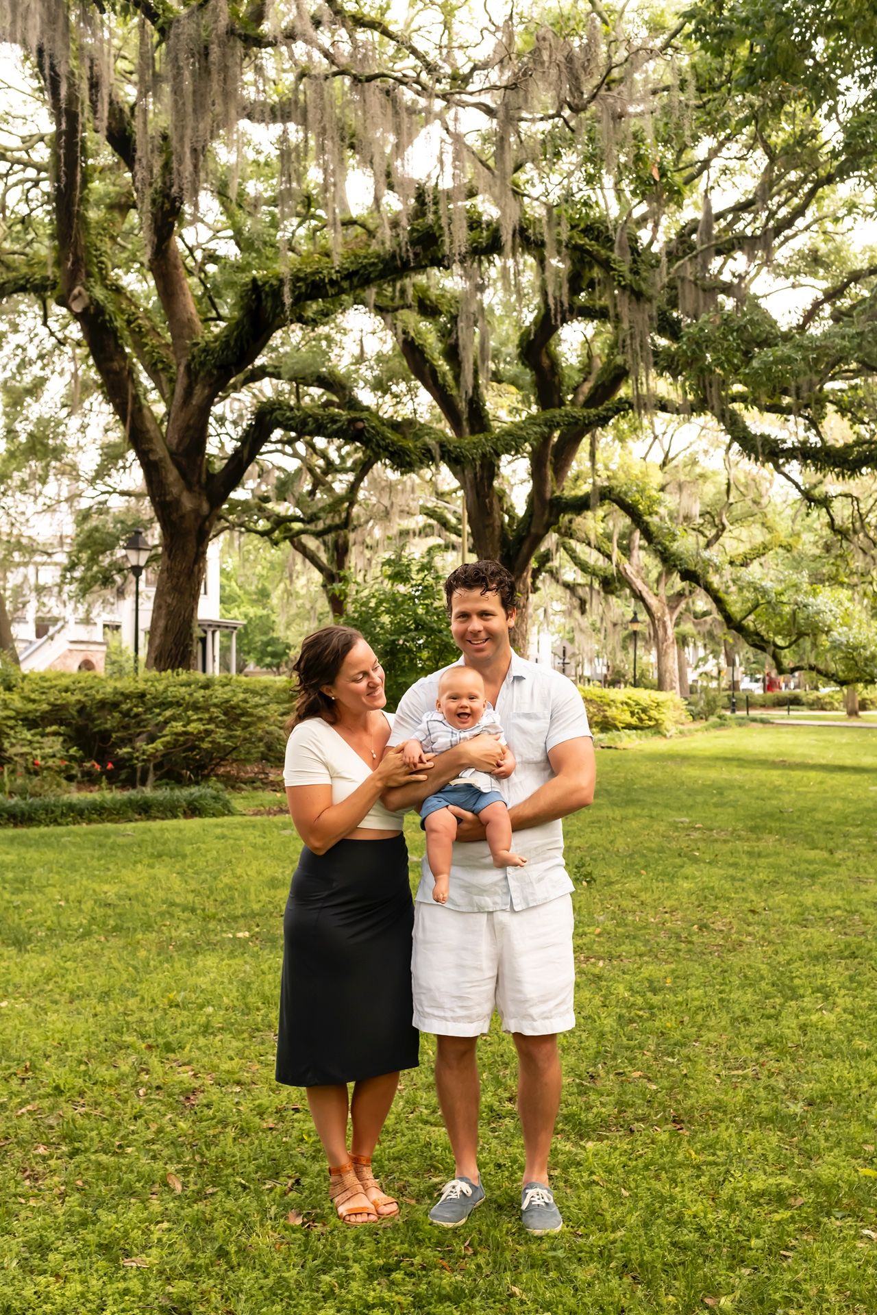 Family having fun and laughing together on grassy lawn with Spanish moss draped trees.