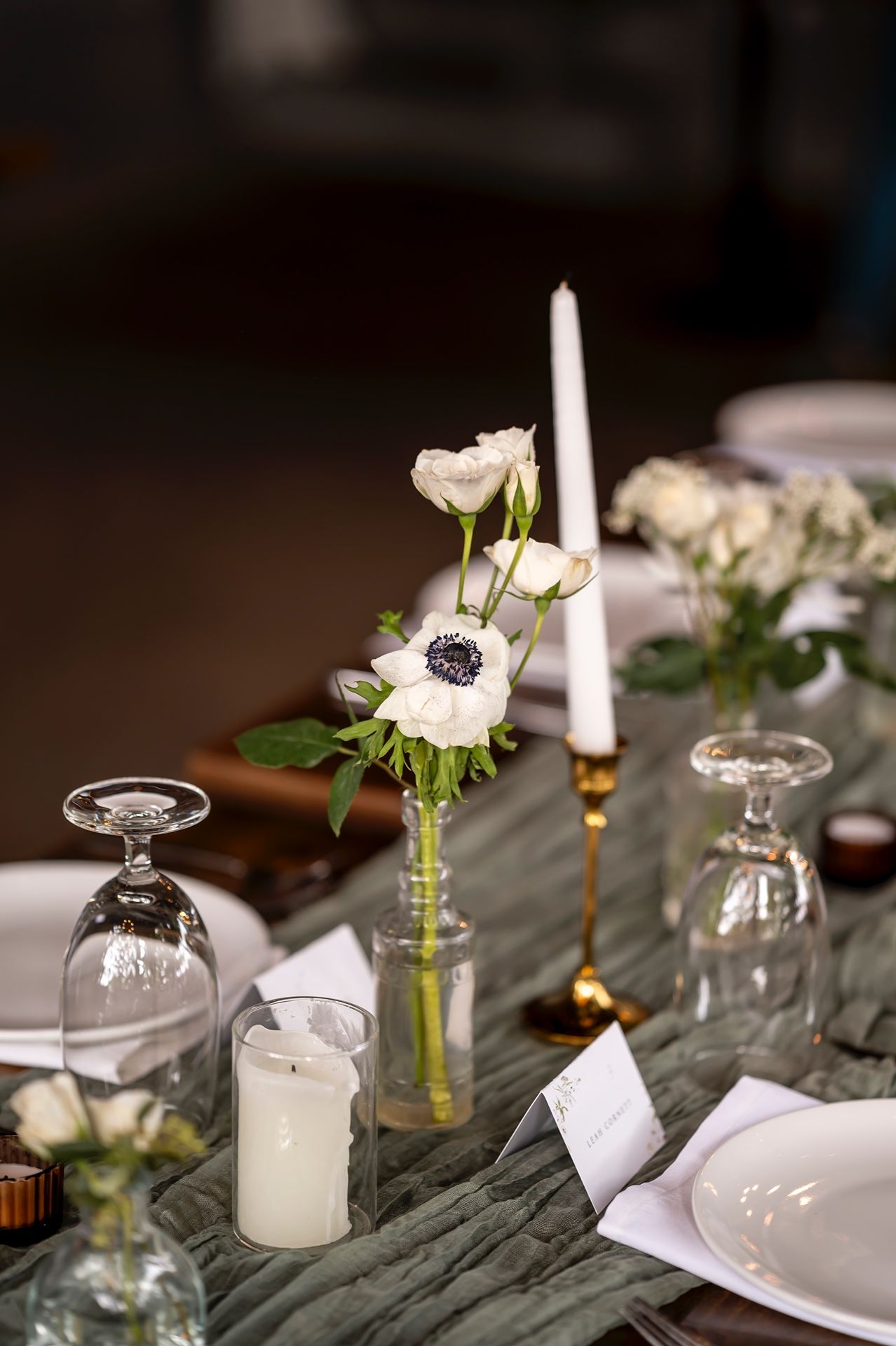 Elegant table setting with white anemone flowers in vase, taper candles, glass domes and textured gray linens.
