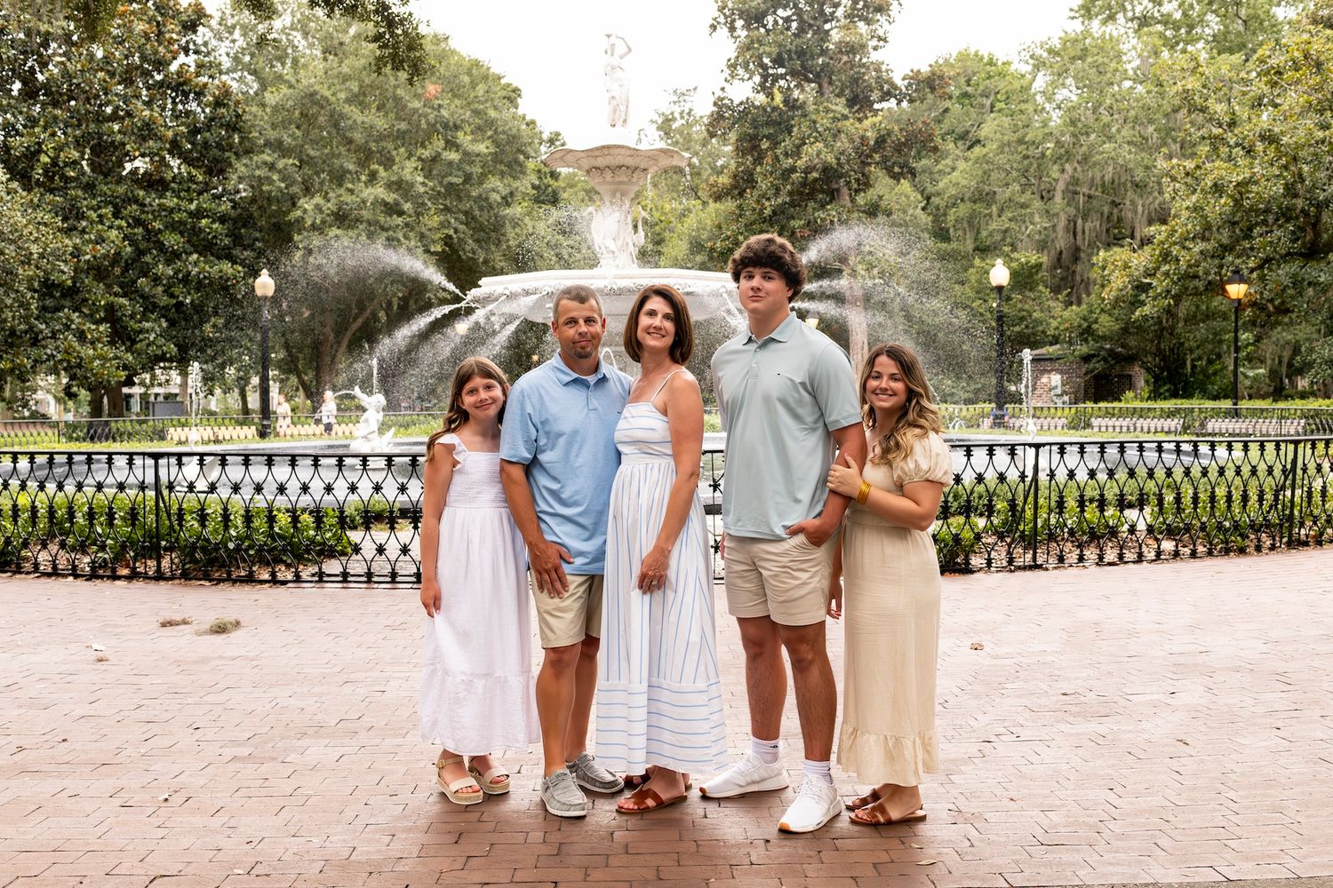 Family members dressed in light colors gather for photos along a white fence in a garden setting.