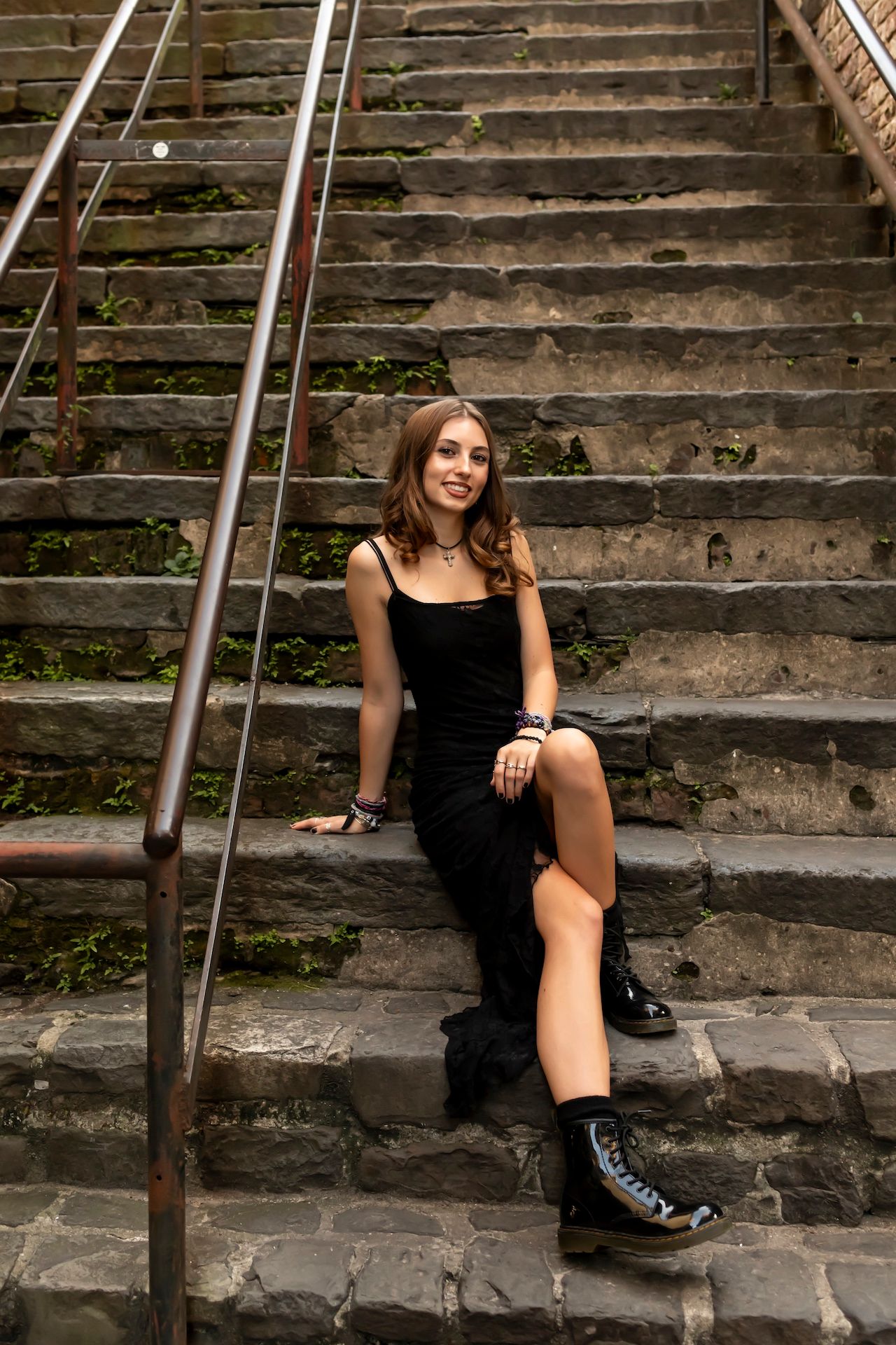 Person in black outfit poses on stone steps with handrail in stylish urban photoshoot series.