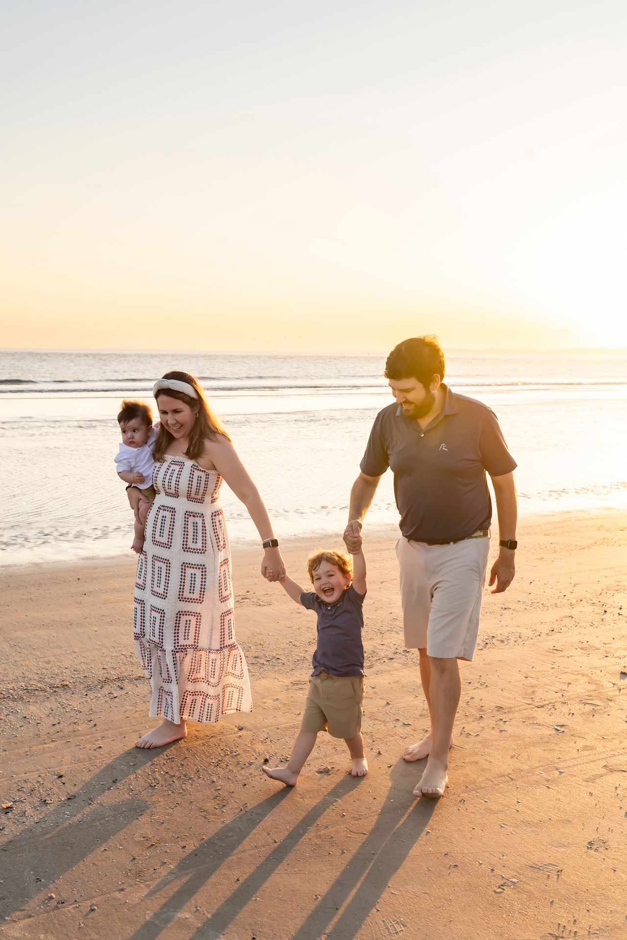 A family walking together along a beach during golden hour, casting long shadows on the sand at sunset.