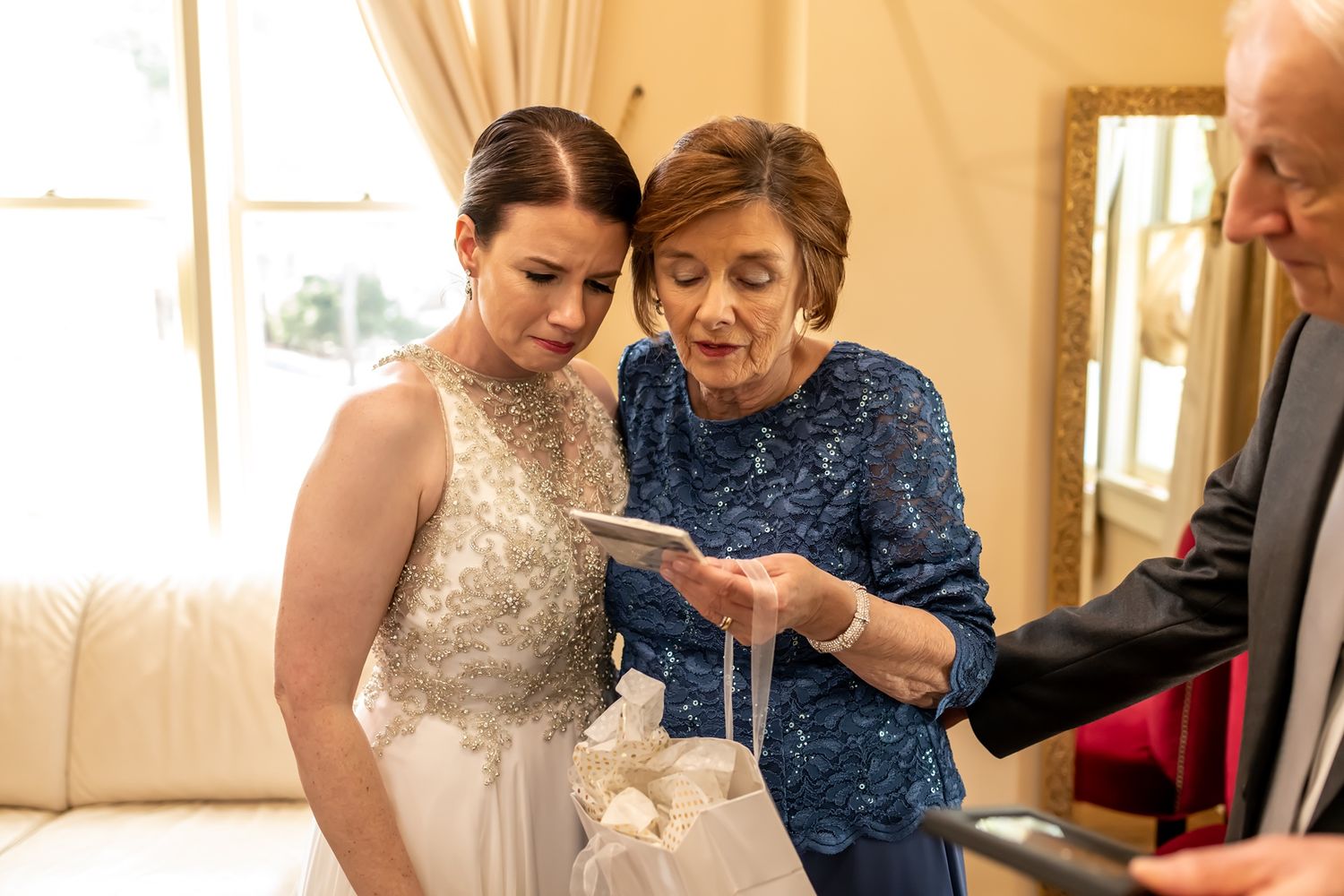 Two people share a tender moment looking at something together on an elegant occasion in a warmly lit room.