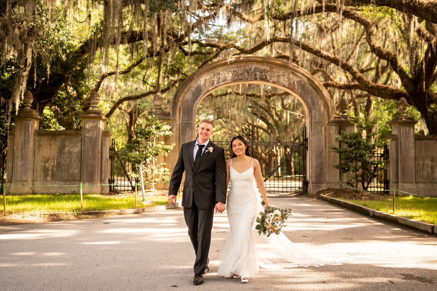 A couple walks under Spanish moss-draped oak trees and stone arches at Wormsloe.