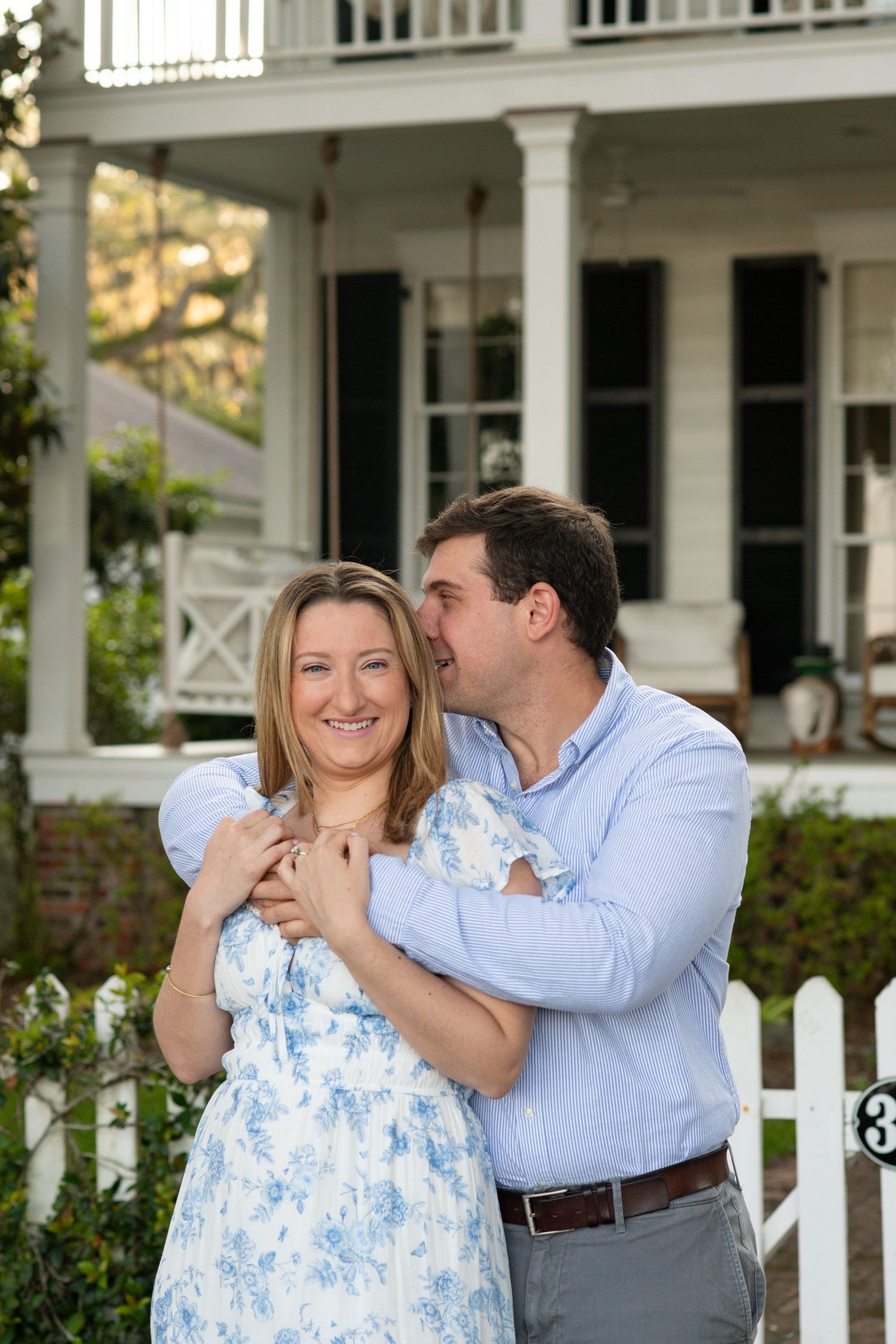 A couple in blue and white outfits share romantic moments together in front of a white porch with picket fence.