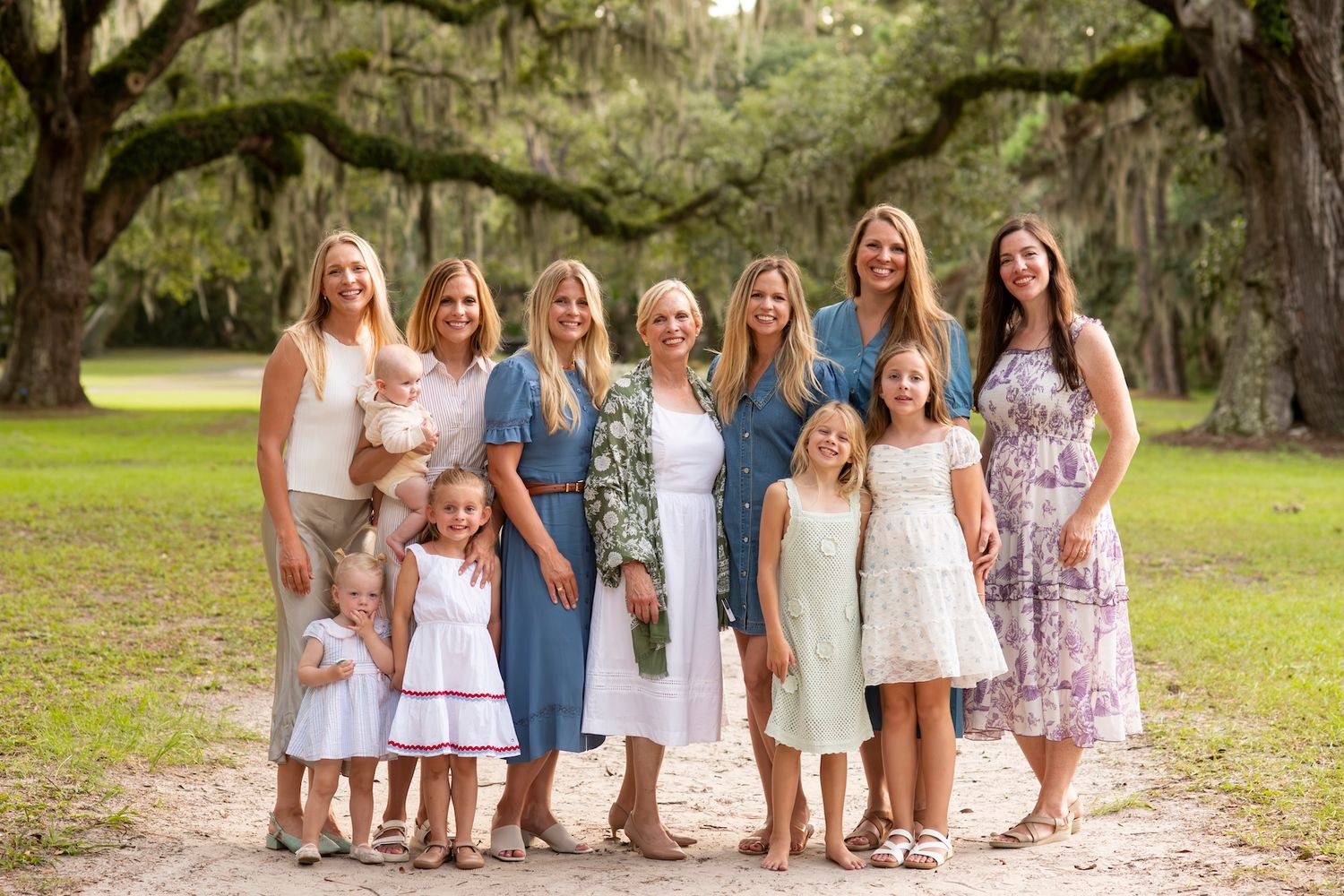 Large family group of women and girls posing outdoors under oak trees on a scenic dirt path.