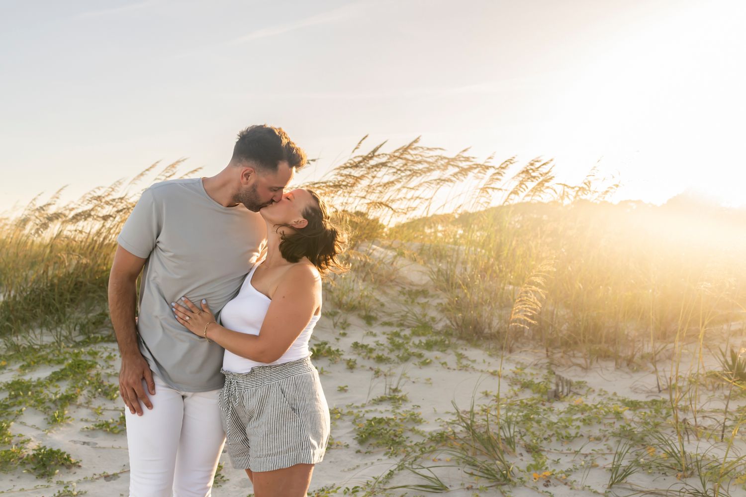 Couple embraces on sandy beach during golden sunset with multiple views of romantic poses along shoreline.