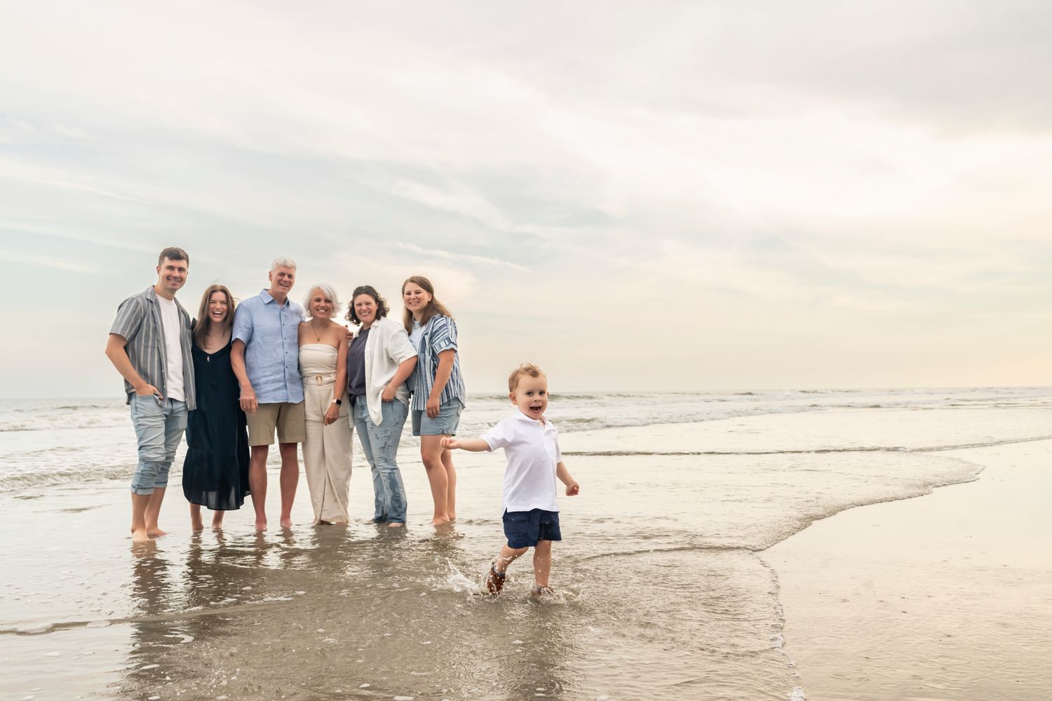 A group of people standing together on a sandy beach at sunset with ocean waves in the background.
