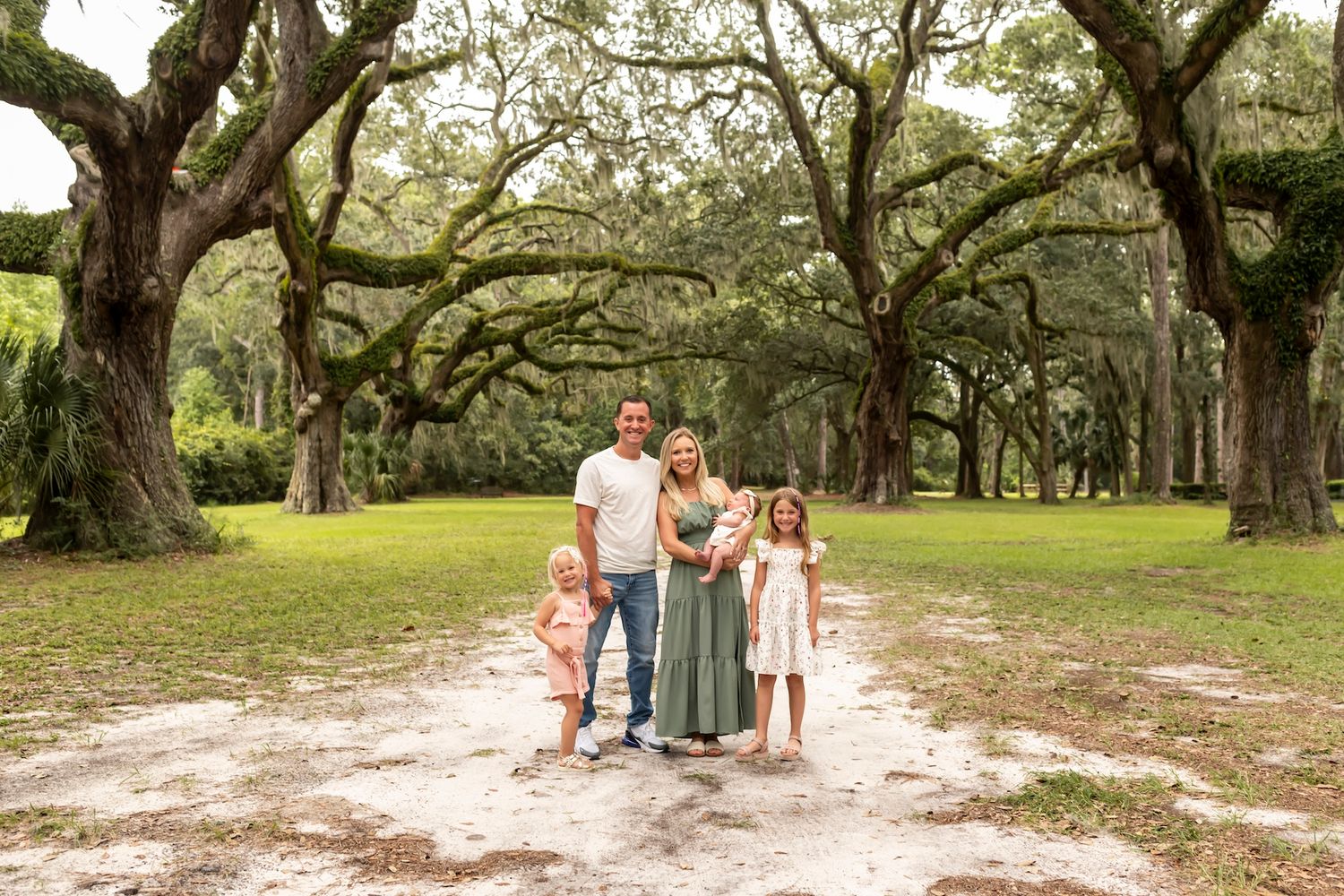 Sprawling live oak trees create a natural canopy over a scenic path in a serene park setting.