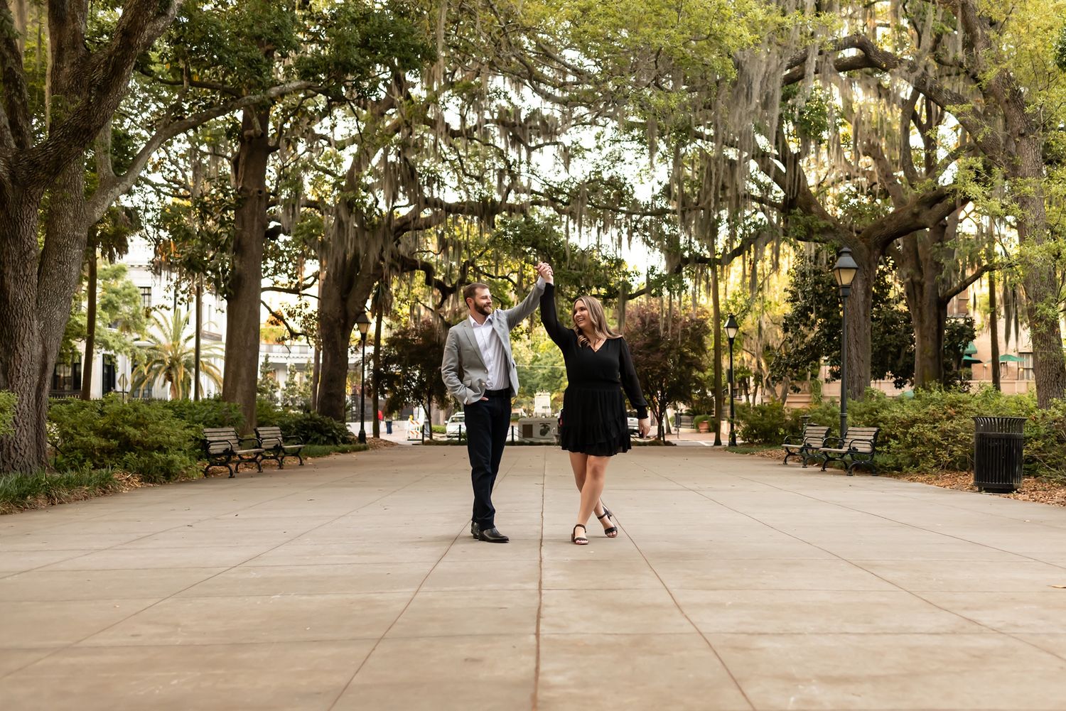 A couple stands together on a tree-lined pathway with Spanish moss hanging from the branches above.