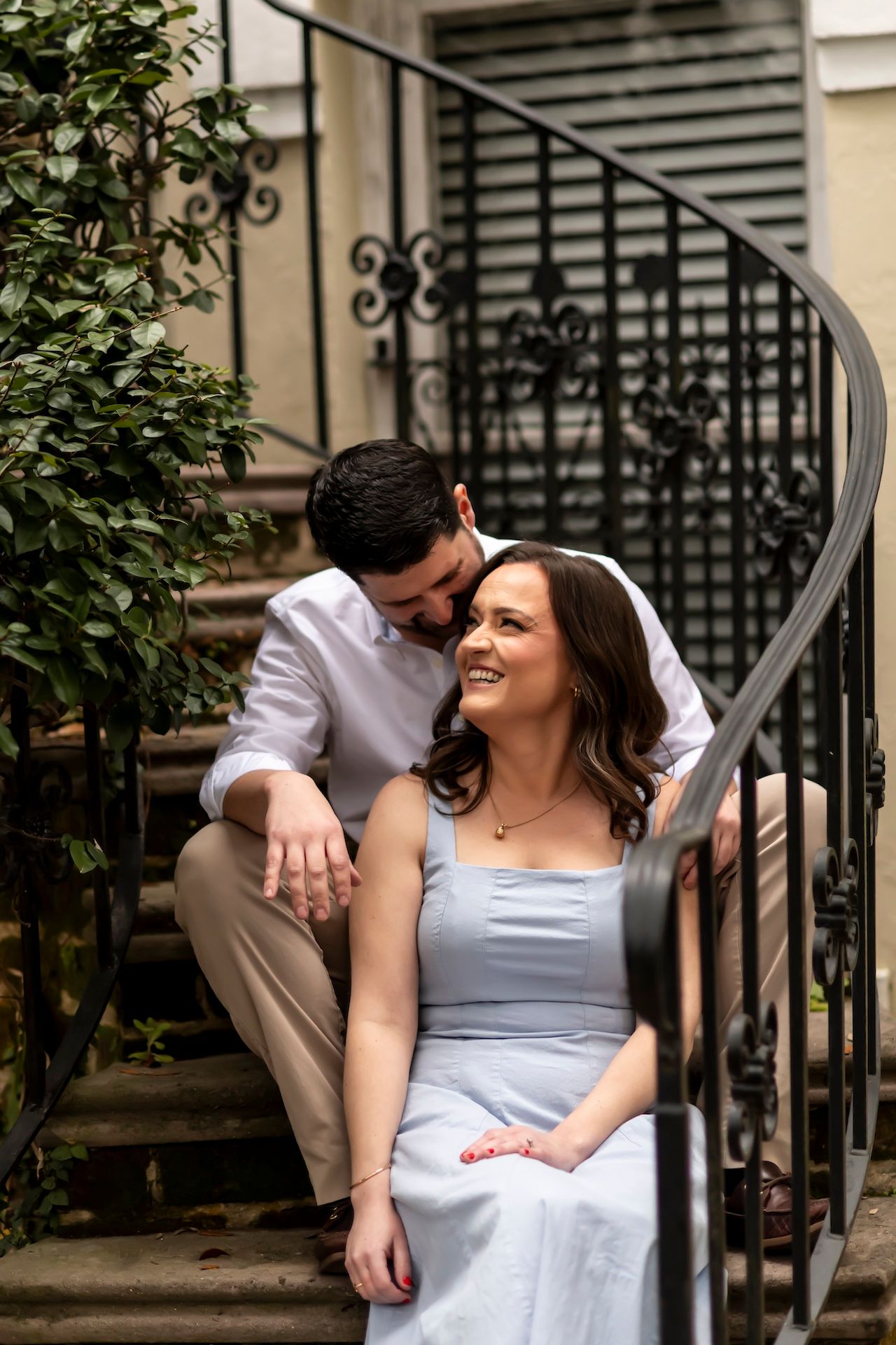 A happy couple shares an intimate moment while sitting on wrought iron stairs outside a brownstone building.