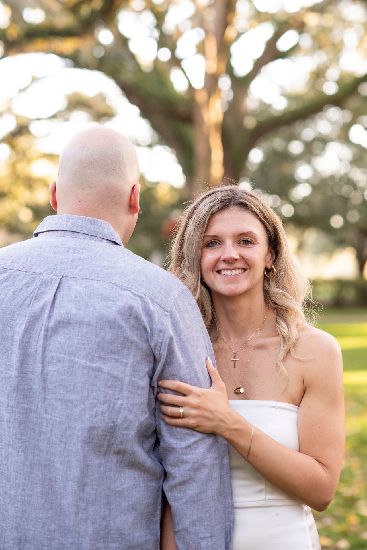 A couple shares an intimate moment outdoors at sunset, with the person on the right wearing a white dress.