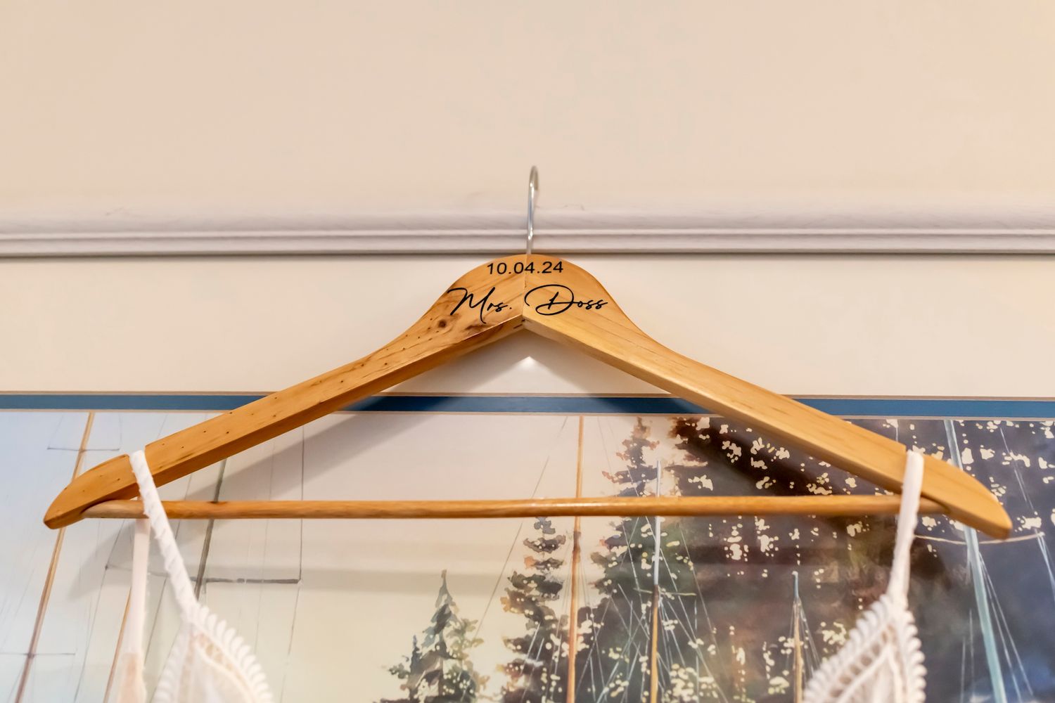 An elegant wooden wedding dress hanger with ornate carved details hangs against a white wall.