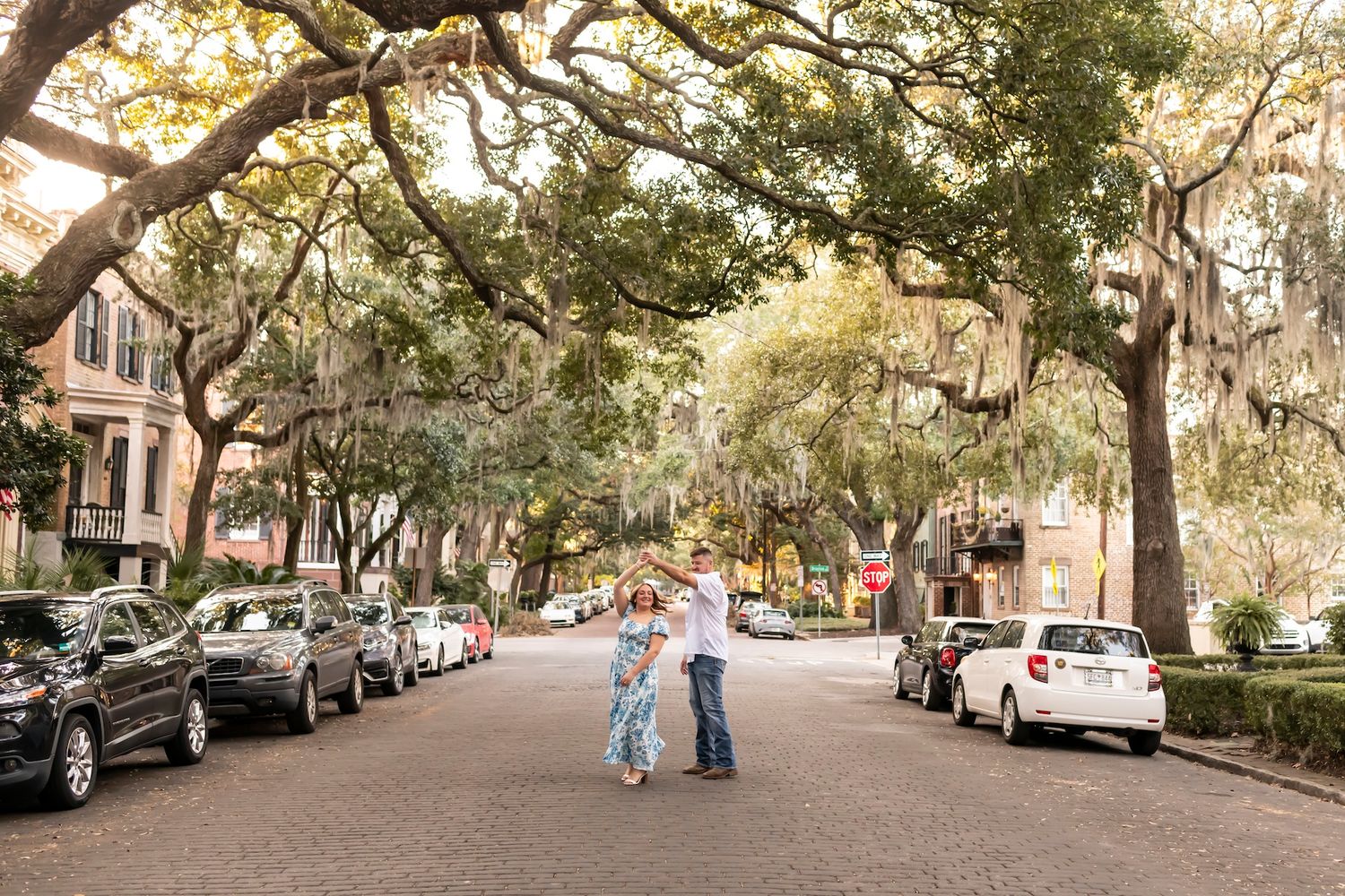 A romantic scene on a tree-lined historic street in Savannah with Spanish moss draping over parked cars.