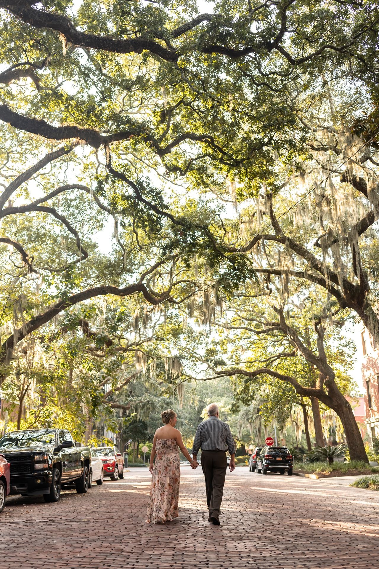 A couple walking down a cobblestone street under a canopy of majestic oak trees draped with Spanish moss in Savannah.