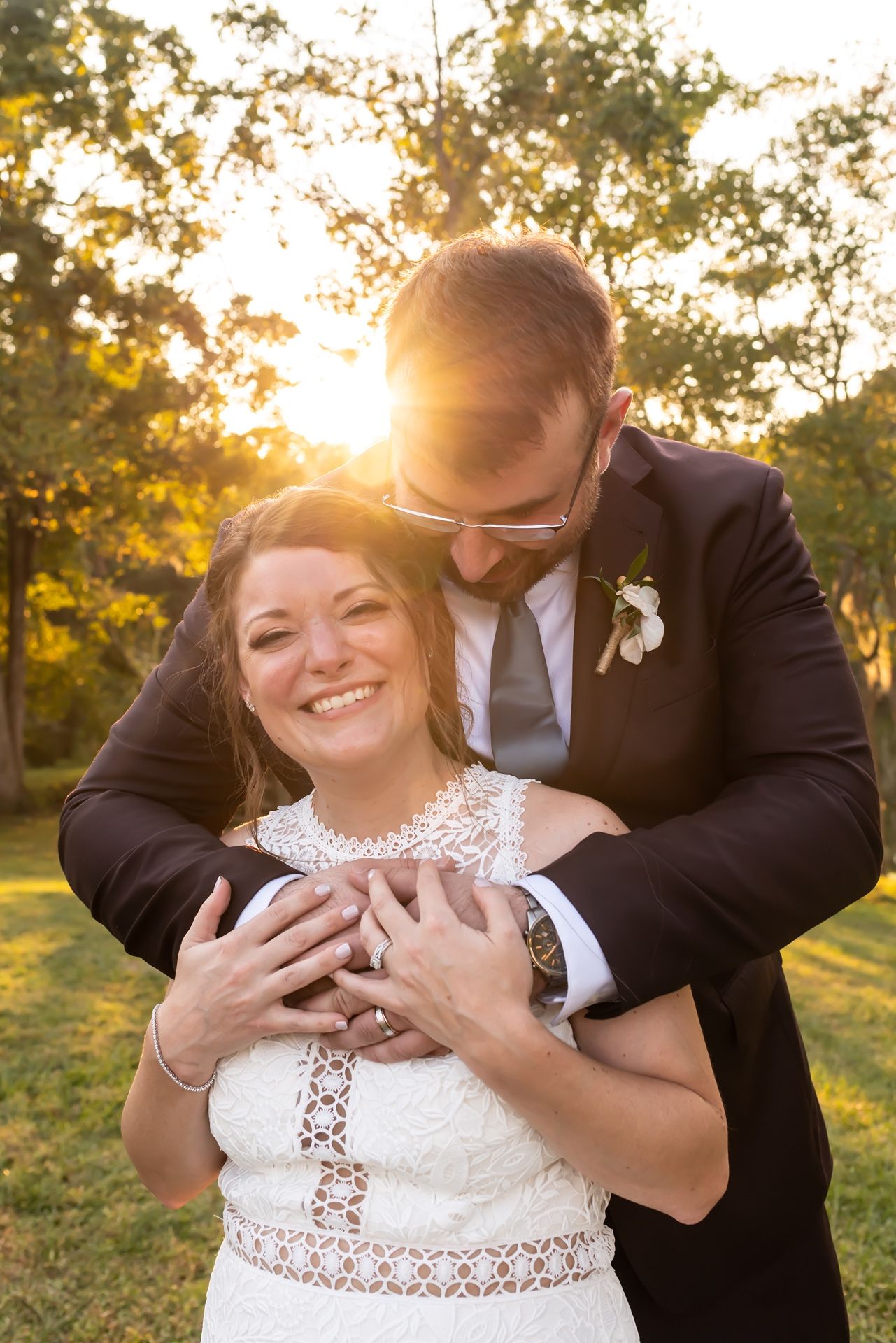 Newlywed couple embracing during golden hour sunset in outdoor garden setting.