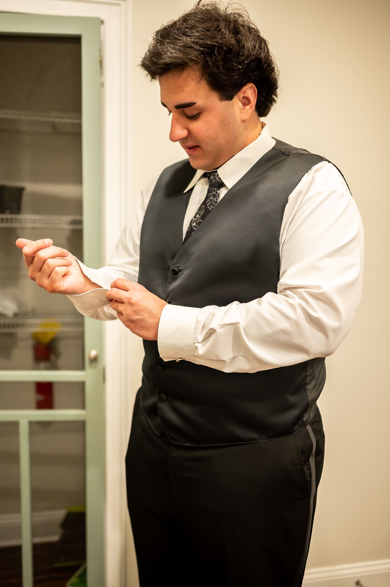 A person in formal attire wearing a dark vest and white dress shirt looks down at an object in their hands.