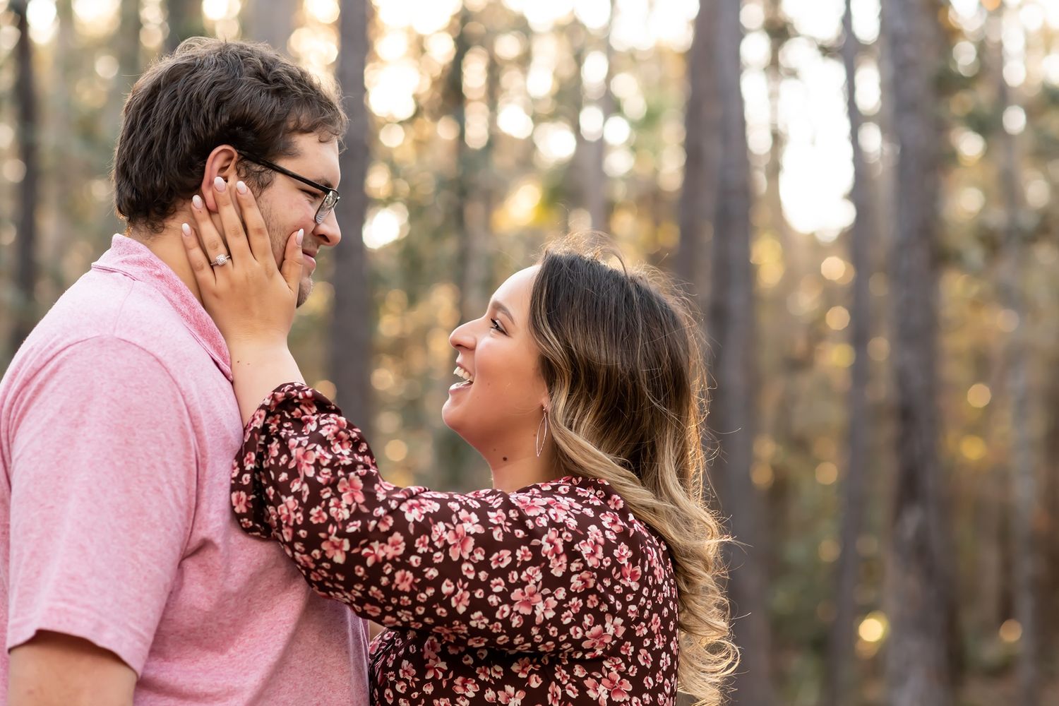 A couple share a loving moment together in a sunlit forest wearing coordinating pink outfits.