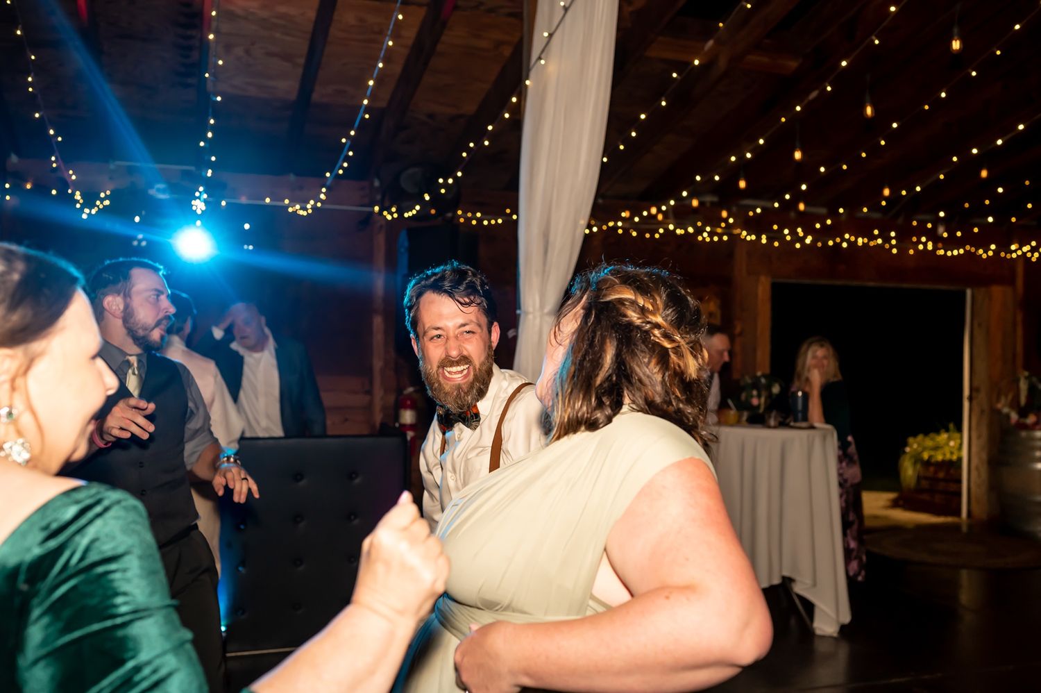 People dancing together at an evening wedding reception under twinkling string lights and blue DJ lighting.