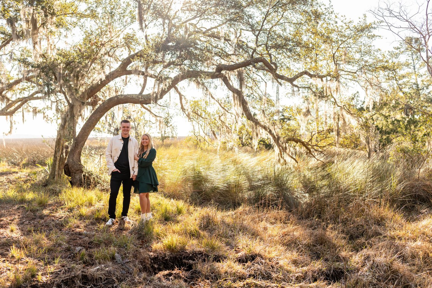 A couple walks along a dirt path through sun-dappled woods during golden hour in the desert landscape.