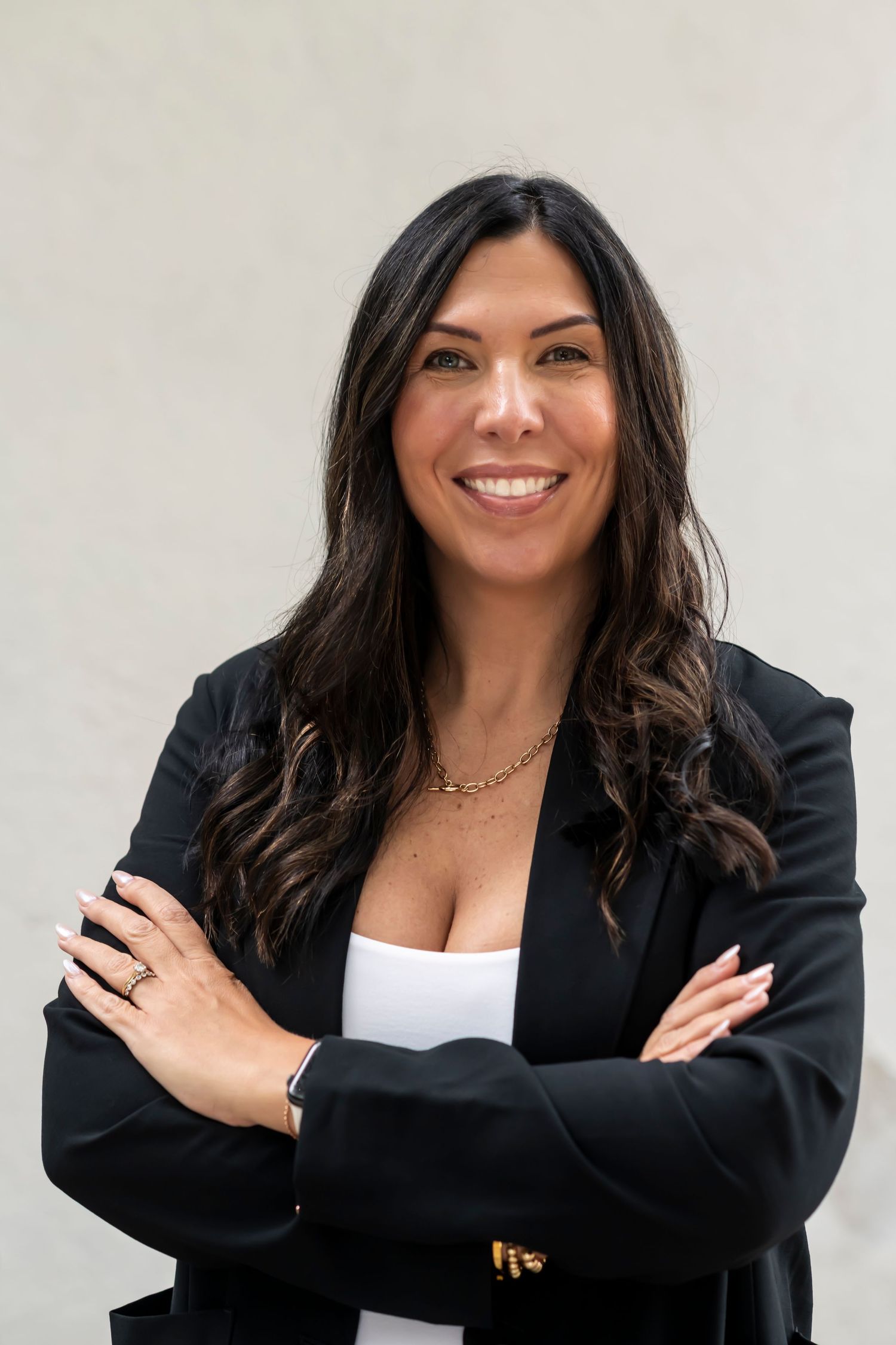 Professional portrait of someone in business attire with long dark hair wearing a black blazer and white top, smiling warmly.