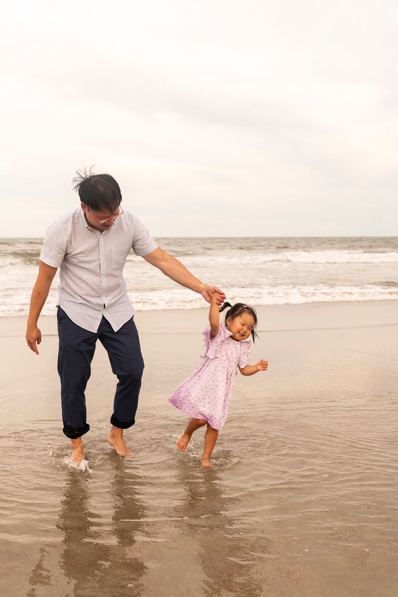 Parent and child play joyfully together in shallow ocean waves at sunset on a peaceful sandy beach.