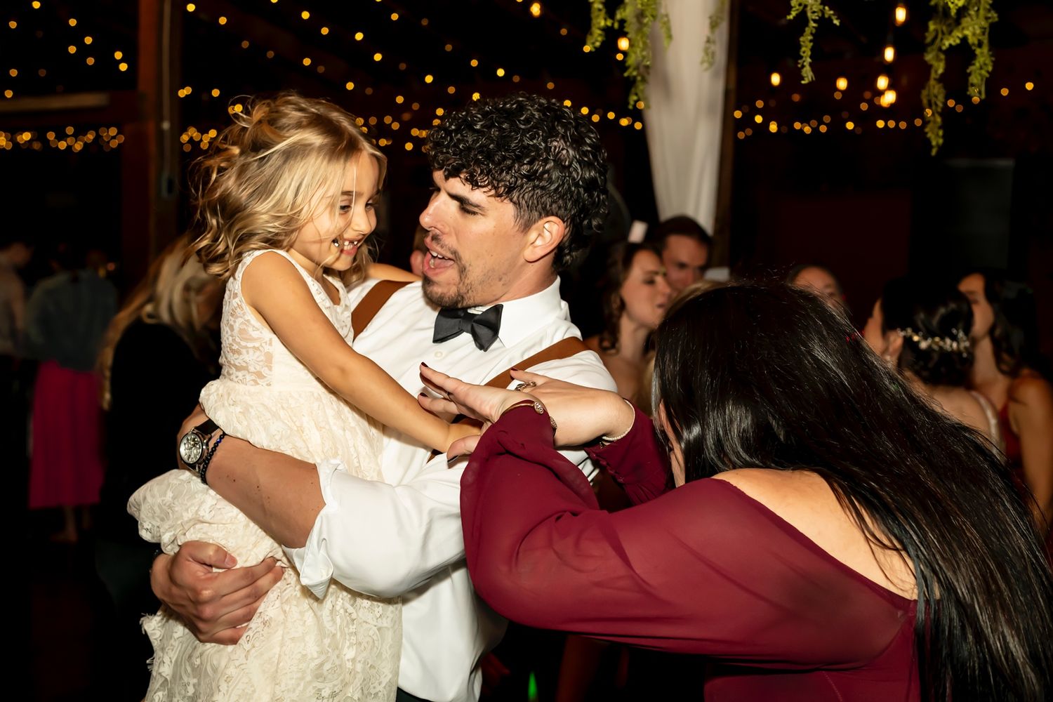 Couples dancing together at a dimly lit reception or party with string lights hanging overhead.