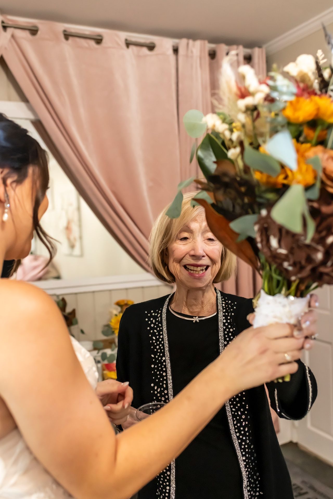 A joyous moment captured at an indoor celebration with floral decorations and beige curtains in the background.