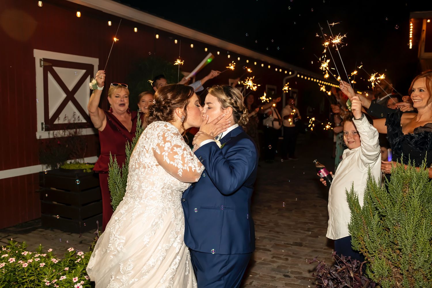 Two people share a romantic dance during an outdoor nighttime wedding celebration with string lights overhead.