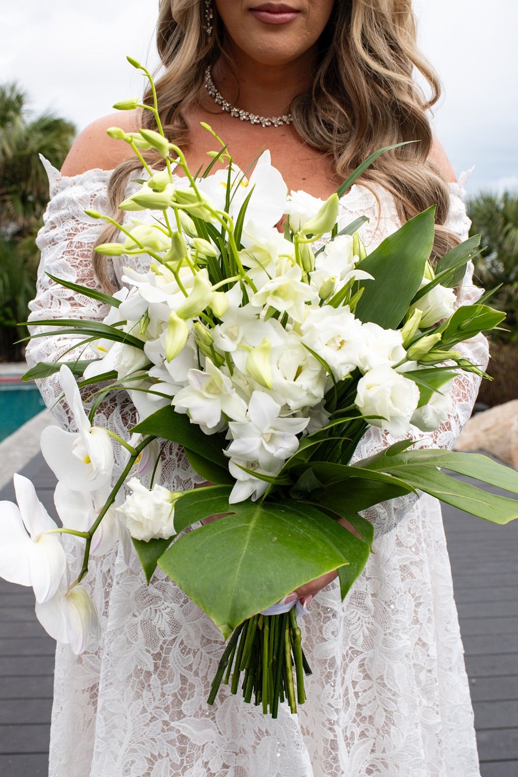 A beautiful white wedding bouquet featuring lilies and greenery held against a lace dress in multiple detail shots.