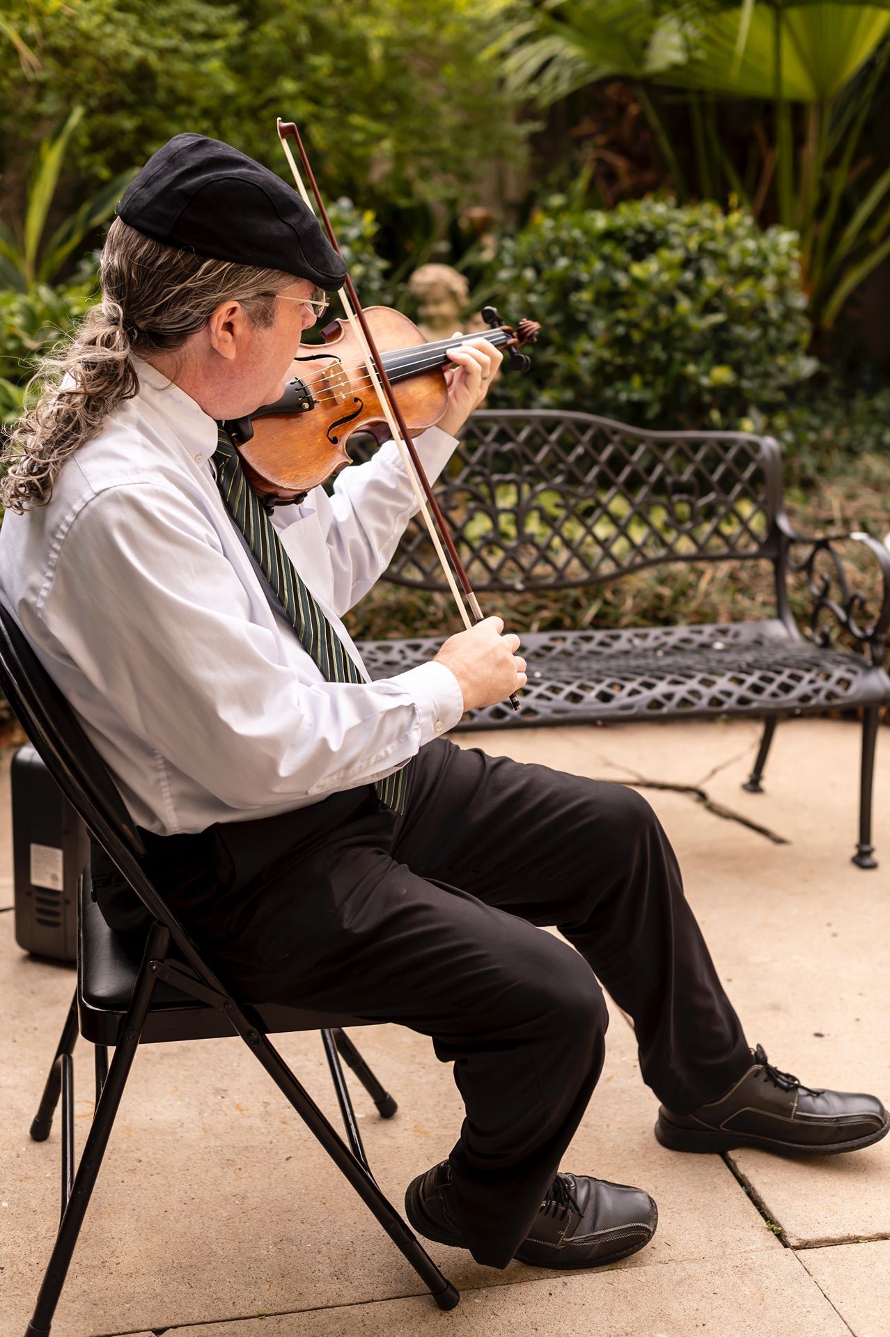 Musicians in black and white attire playing violins while seated in outdoor chairs.